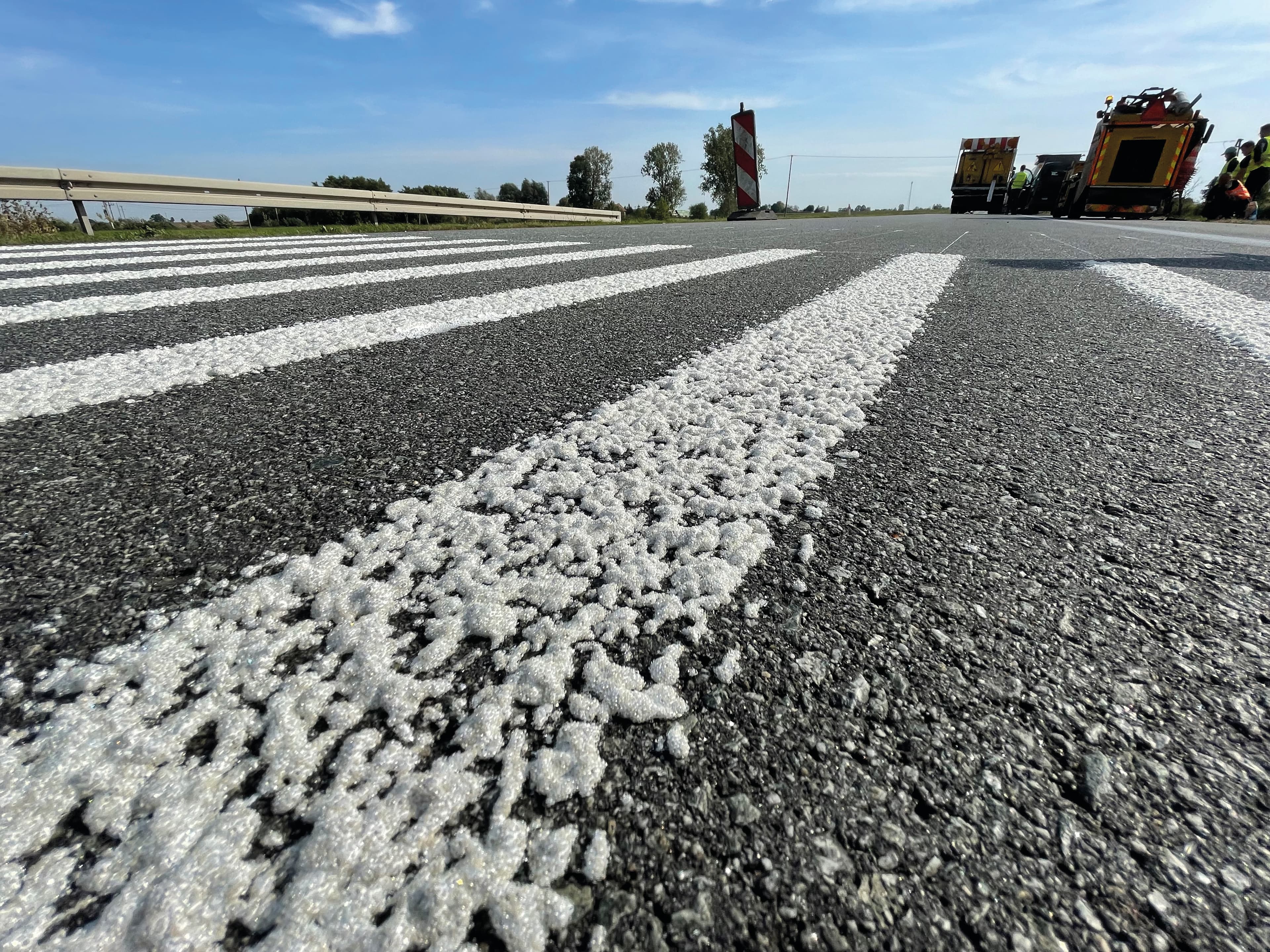 Weiße Fahrbahnmarkierung auf Asphalt mit sichtbar eingestreutem Nachstreumittel für hohe Sichtbarkeit und Griffigkeit im Straßenverkehr