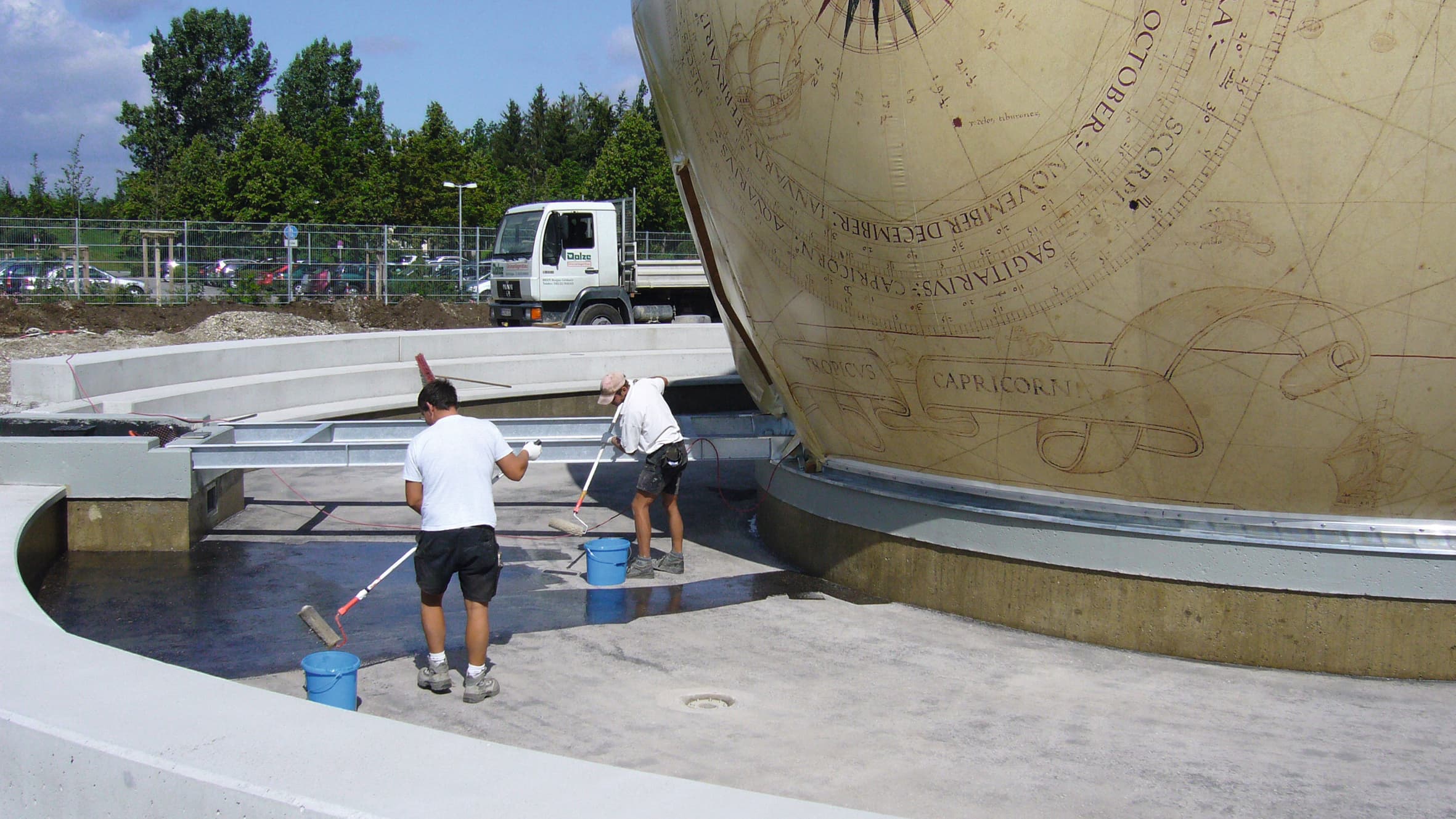 Workers are cleaning and maintaining the water feature surrounding a large, intricately engraved globe in a modern outdoor setting.