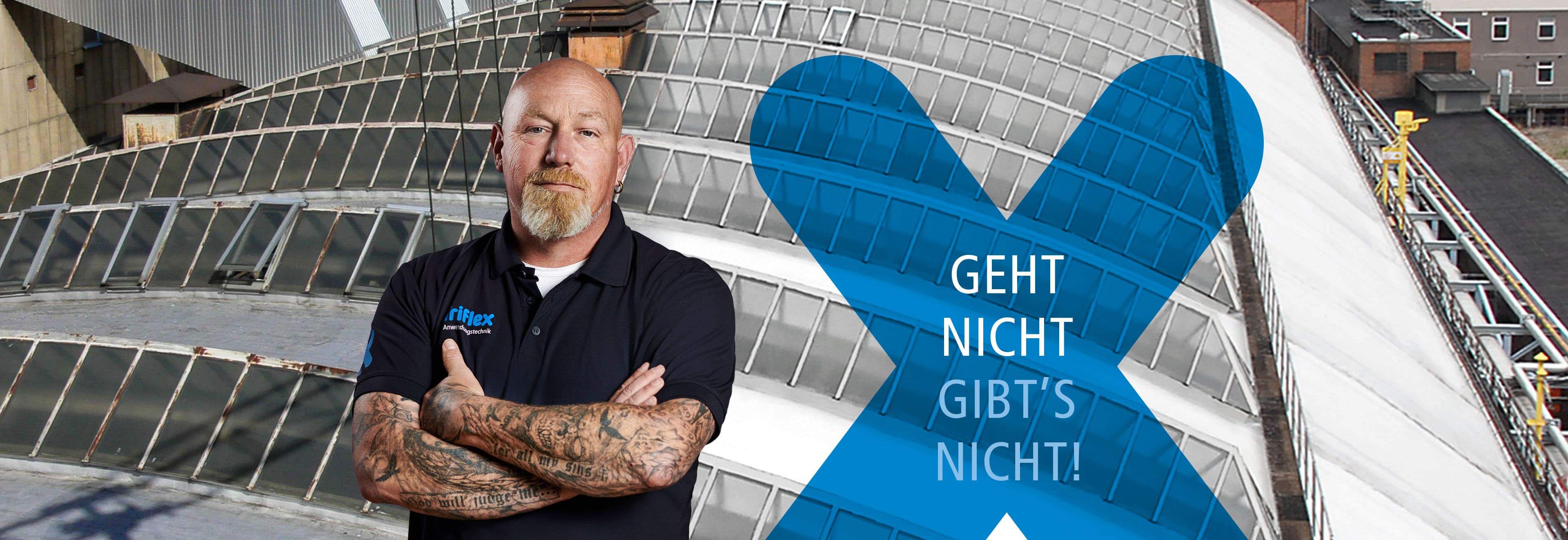 Dachdecker steht vor einem Industriedach mit verschränkten Armen und Kampagnenbotschaft „Geht nicht gibt’s nicht“