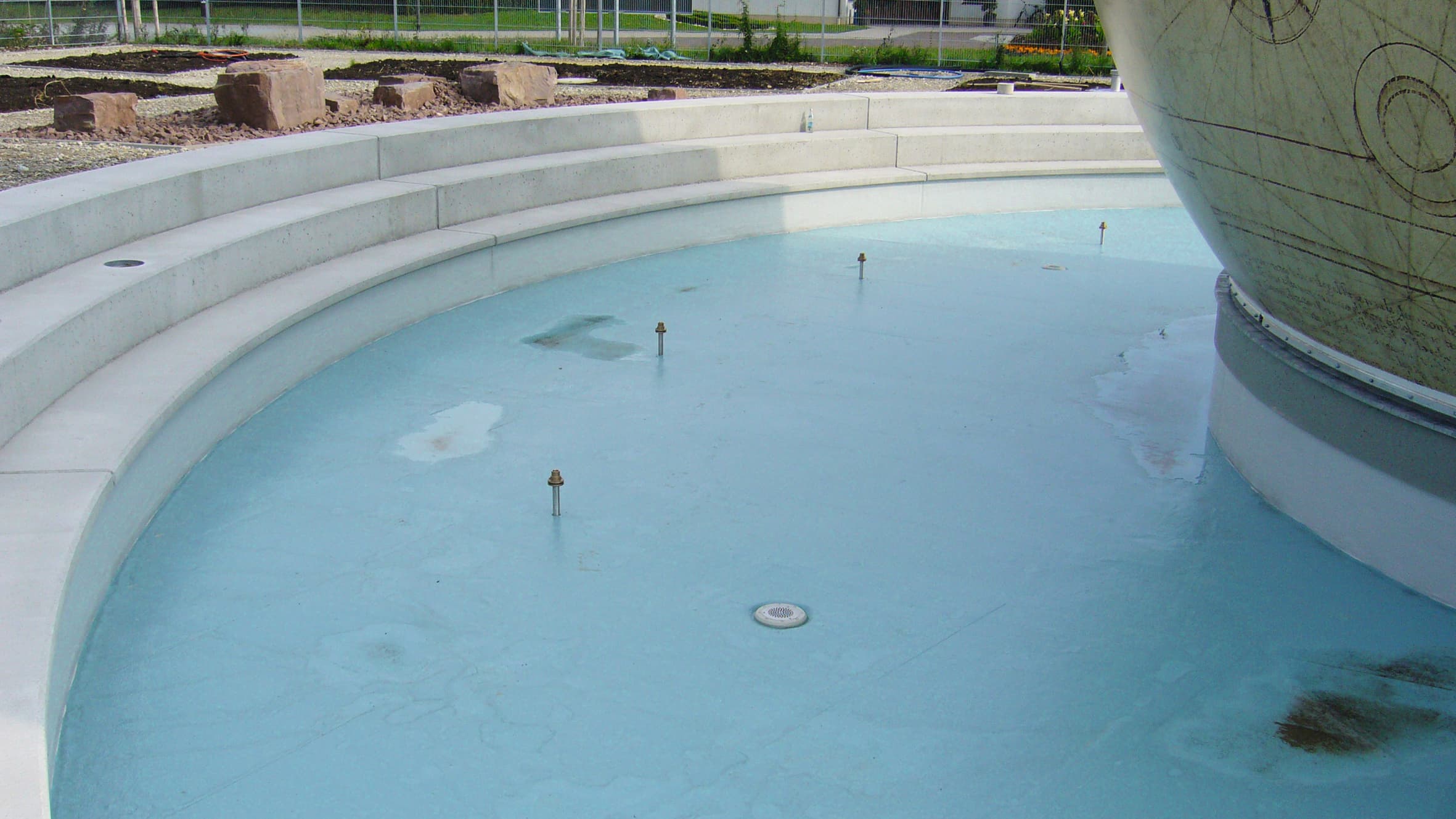 A water feature in an outdoor space with a light-colored terrace structure and a decorative globe, part of a landscaped outdoor area.