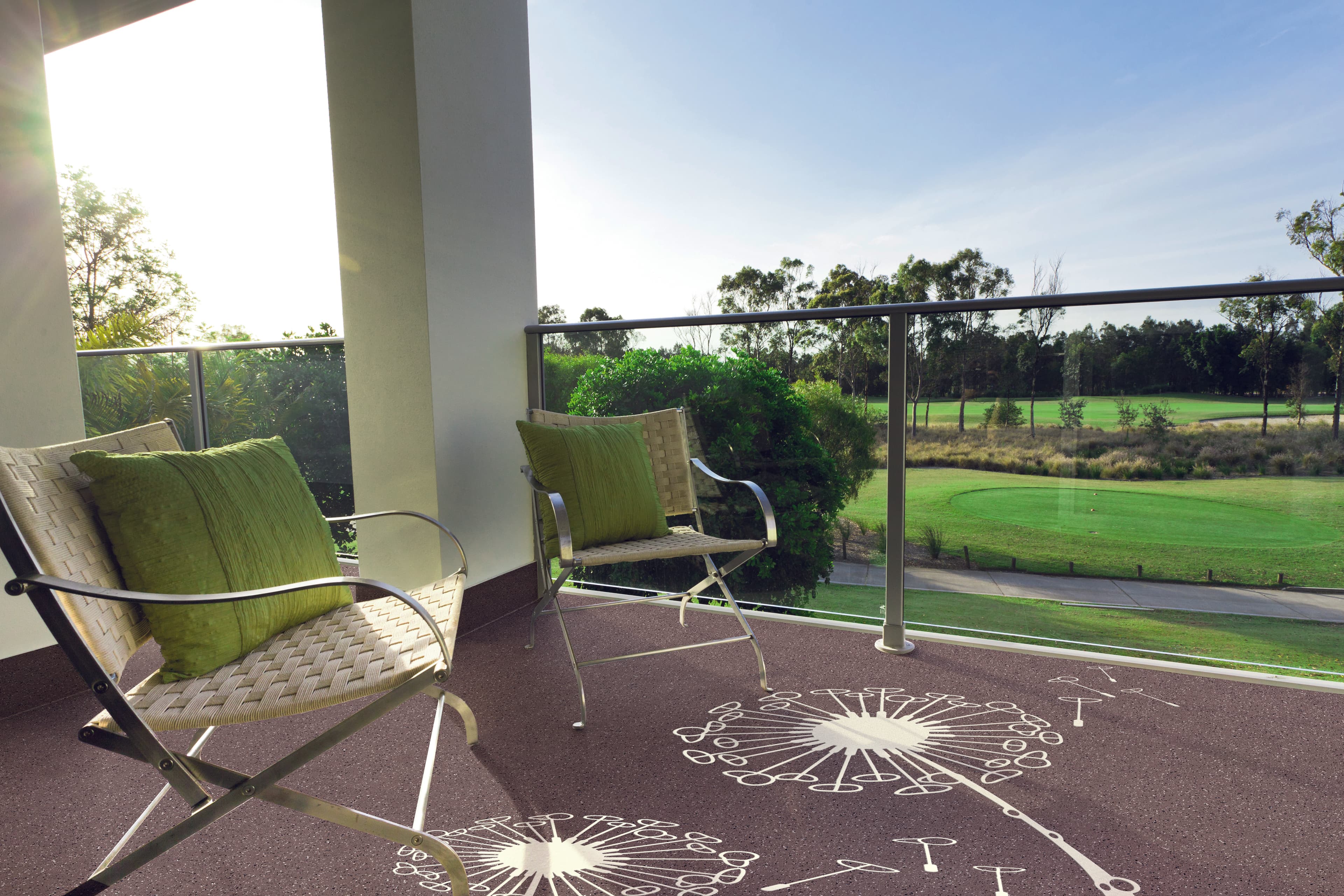 Balkon mit Triflex Floor Tattoo Design „Pusteblume“ auf dekorativ beschichtetem Bodenbelag, zwei Sitzstühle mit grünen Kissen und Blick auf eine Park- bzw. Golfanlage