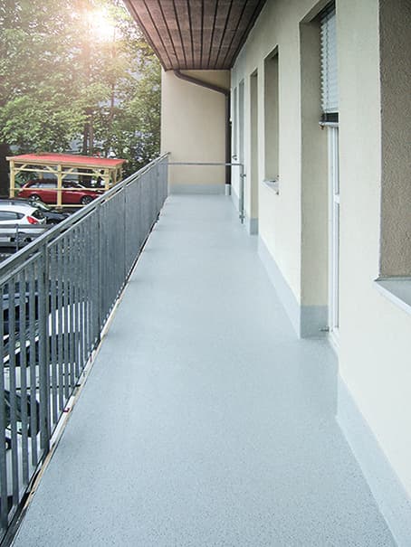 A renovated balcony pergola on a residential building featuring a slip-resistant, light gray coating and metal railings for long-lasting outdoor use.