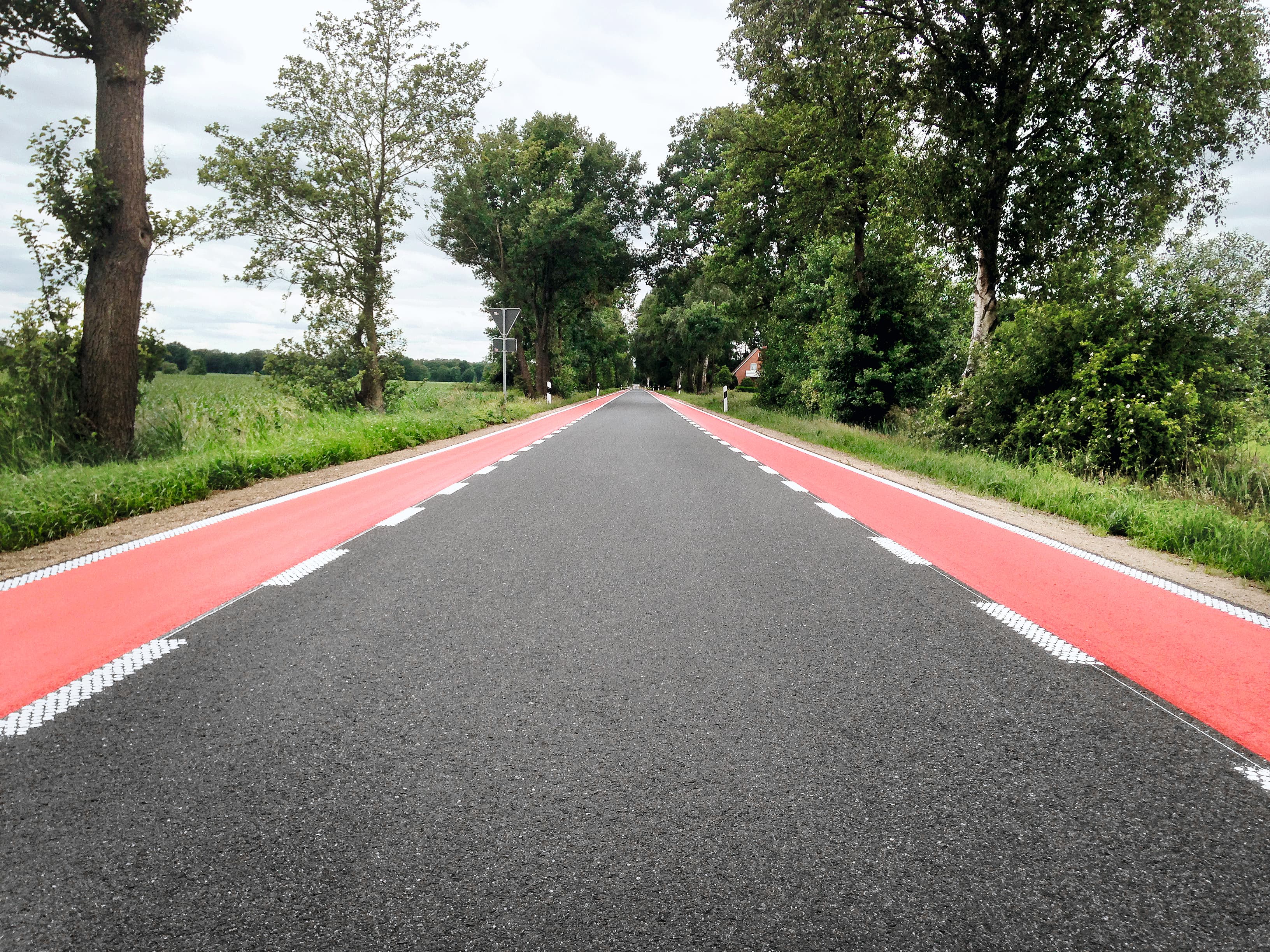 Renovated country road with red edge markings for bicycle traffic—a durable road surface coating on asphalt to ensure safe routing in rural areas.