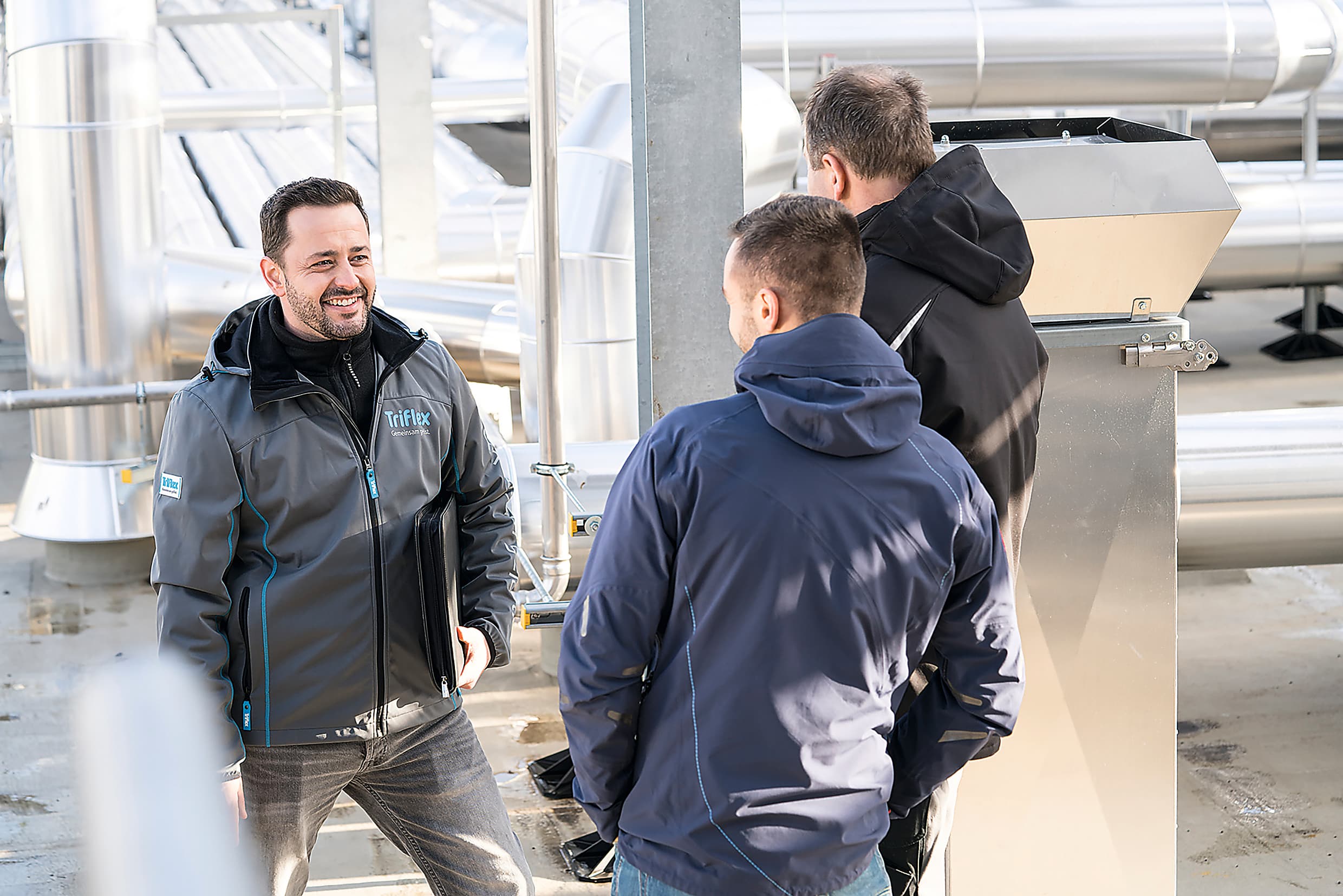 Fachlicher Austausch von Mitarbeitenden auf einem technischen Dachaufbau mit Leitungsanlagen