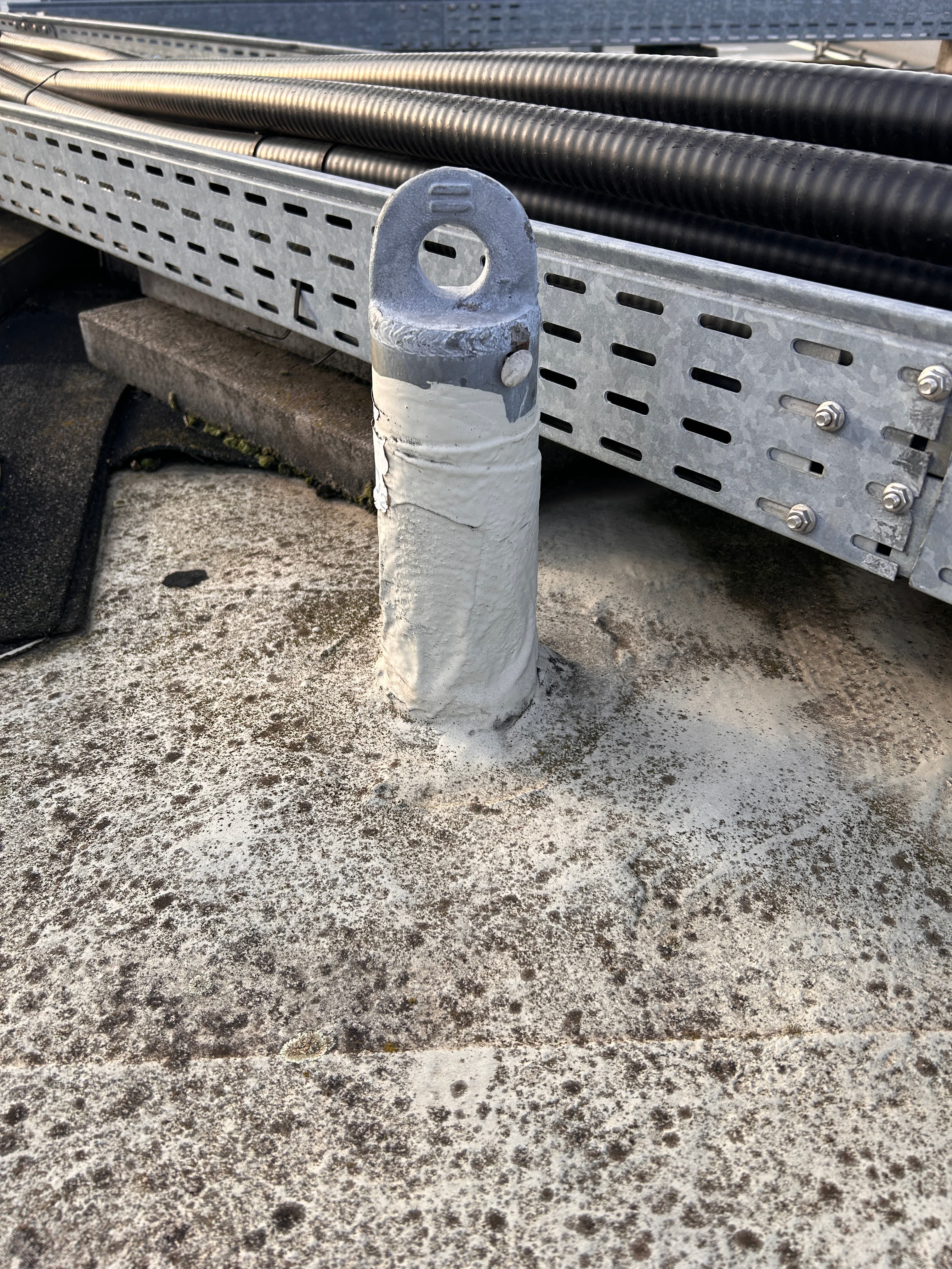 Abgedichteter Dachanschluss mit metallischer Befestigungsöse auf einer Flachdachfläche in Minden, umgeben von Kabel- und Trassenleitungen.