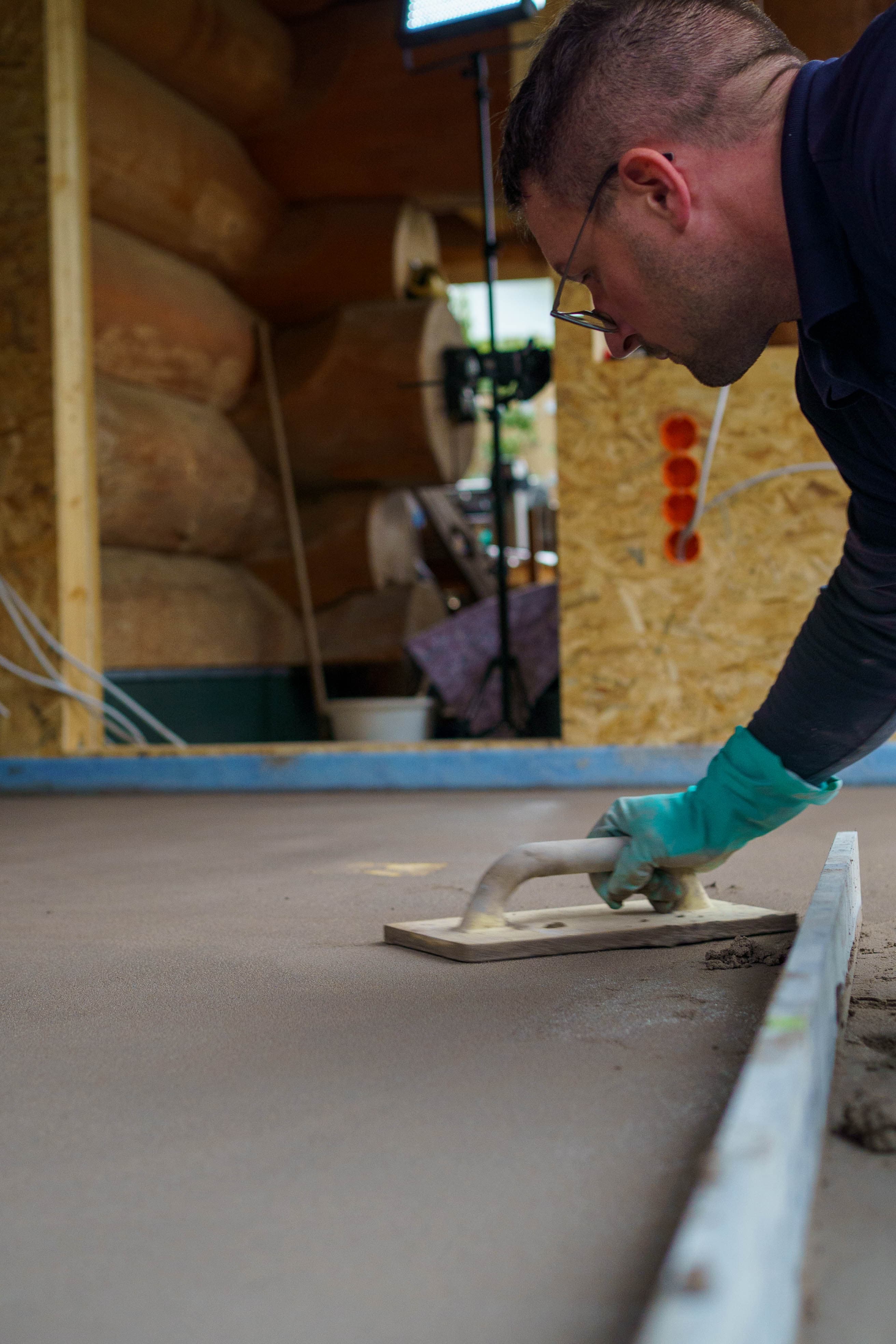 A contractor smooths the screed surface with a trowel on a construction site