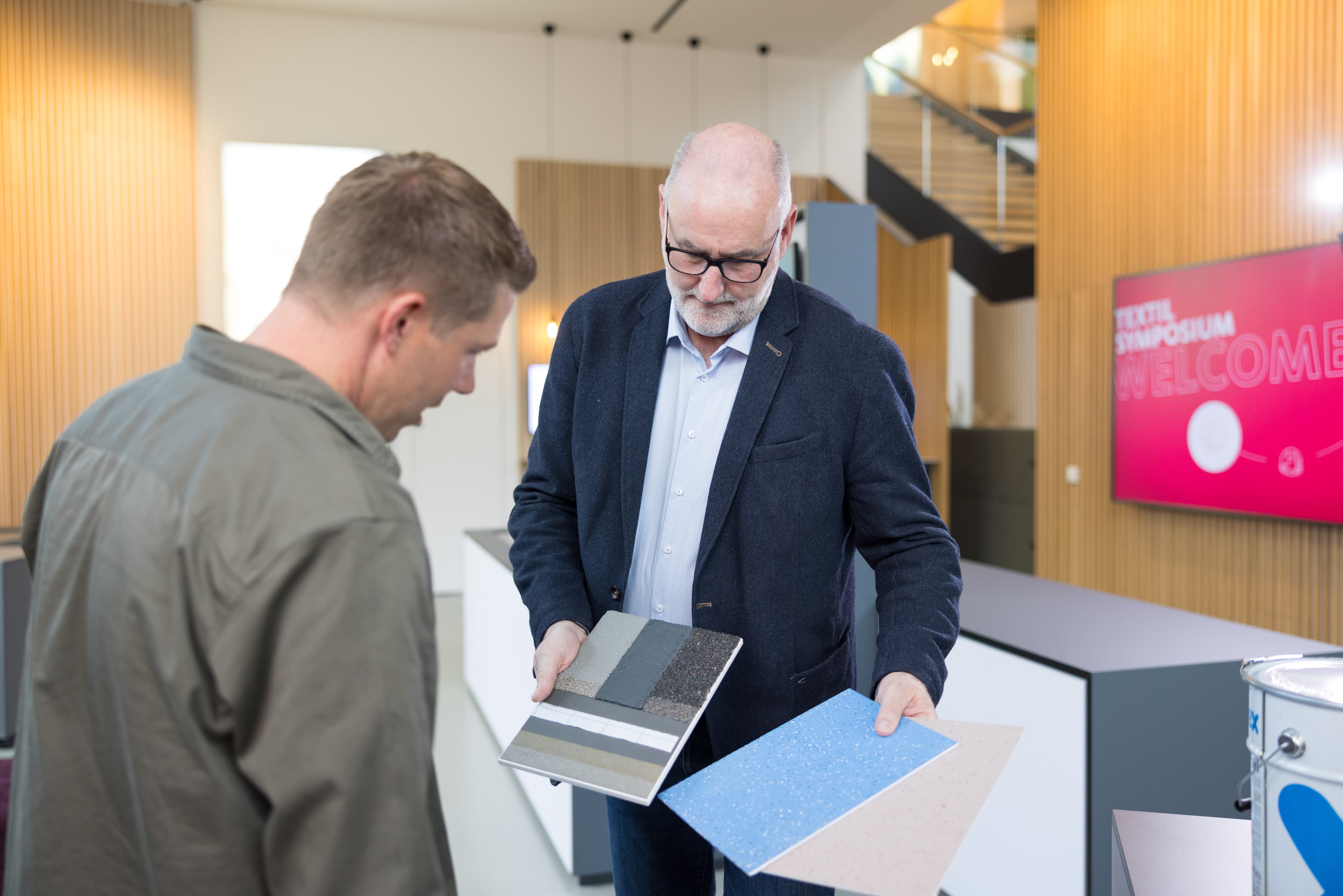 Beratungssituation im modernen Ausstellungs‑ und Empfangsbereich, bei der verschiedene Material‑ und Farbmuster für Oberflächenlösungen vorgestellt und verglichen werden.