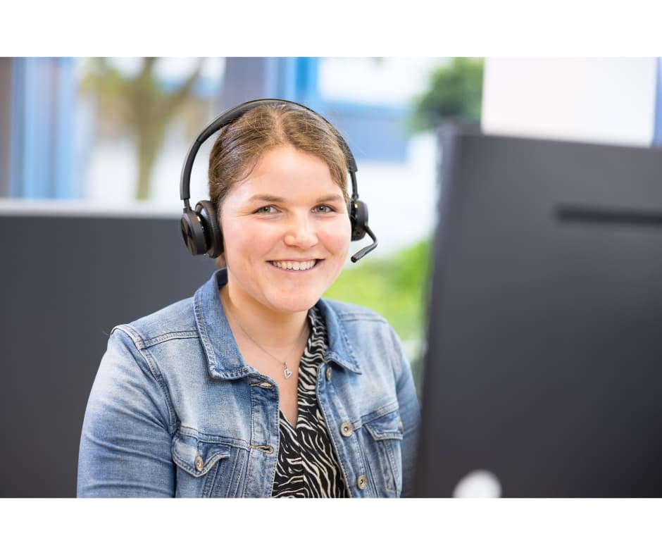 Mitarbeiterin mit Headset sitzt am Computer und berät telefonisch im Kundenservice.