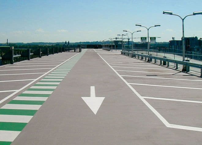 Verkehrsflächenmarkierung auf einem Parkdeck mit weißem Fahrtrichtungs‑Pfeil und grün markiertem Fahrstreifen – strukturierte Parkhauslösung