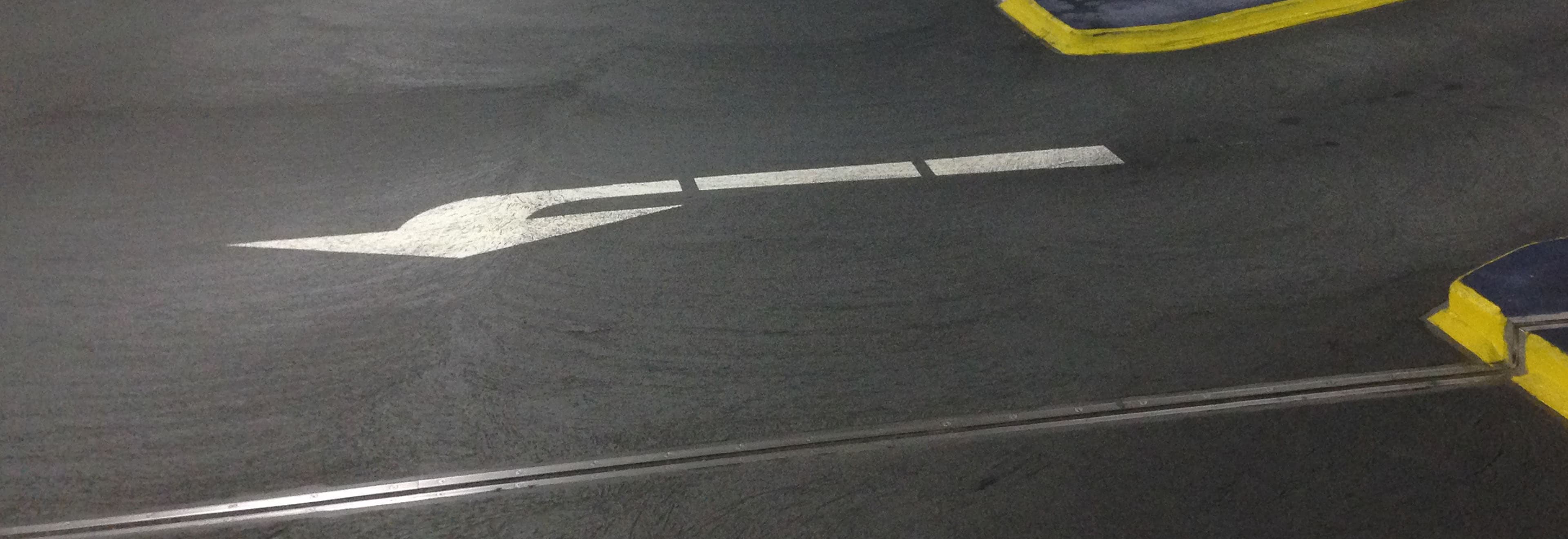 A coated roadway in an underground parking garage with white directional markings and yellow-marked edge areas.