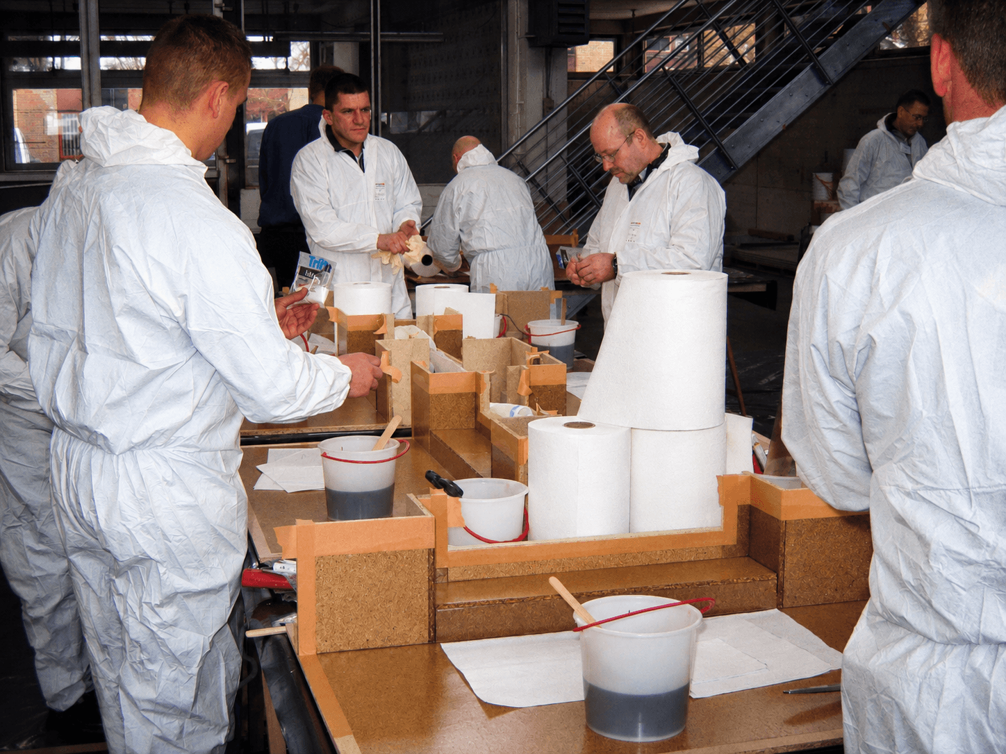 Teilnehmer arbeiten im Praxisseminar an einem Tisch mit Modellen, Werkzeugen und Triflex Materialien an praktischen Abdichtungsaufgaben.