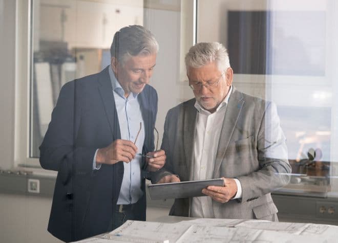 Architekt und Planer besprechen Bauplanung anhand von Zeichnungen und Tablet
