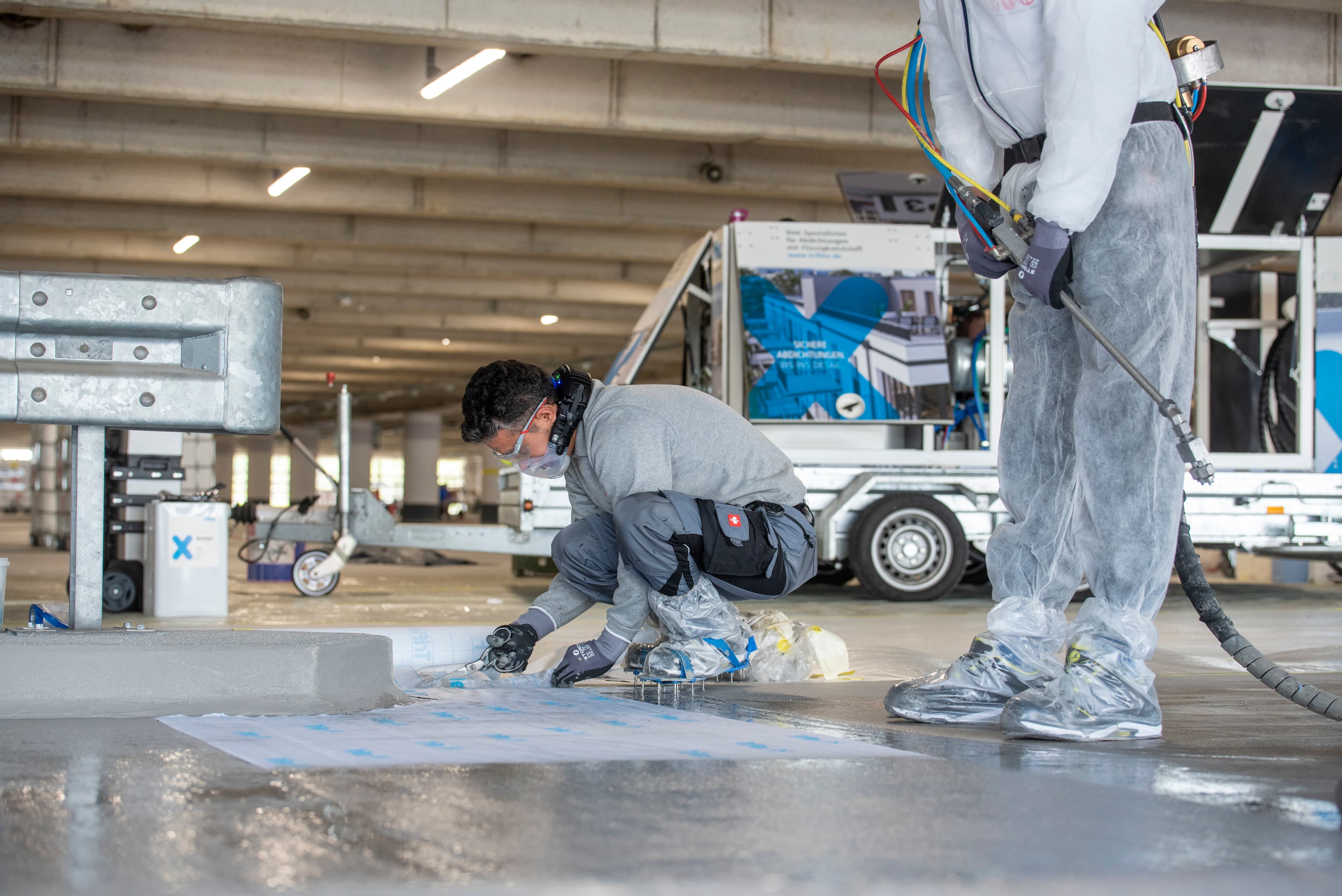 Verarbeitung einer flüssig aufgetragenen Bodenbeschichtung durch Fachkräfte auf einer Verkehrsfläche in einem Parkhaus oder einer Industriehalle.