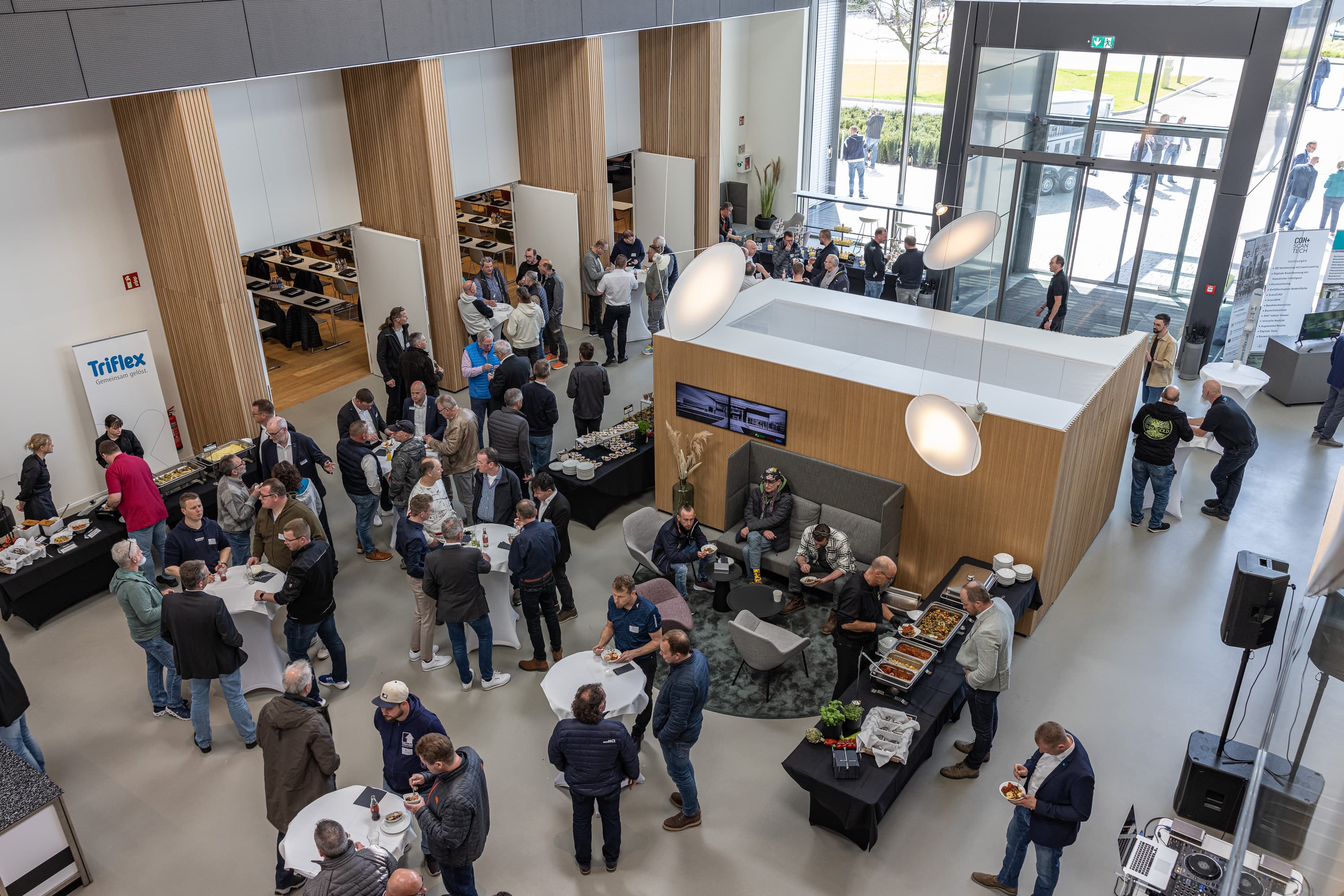 People at an event in the lobby of a modern office building with a reception area, seating areas, and a glass facade.