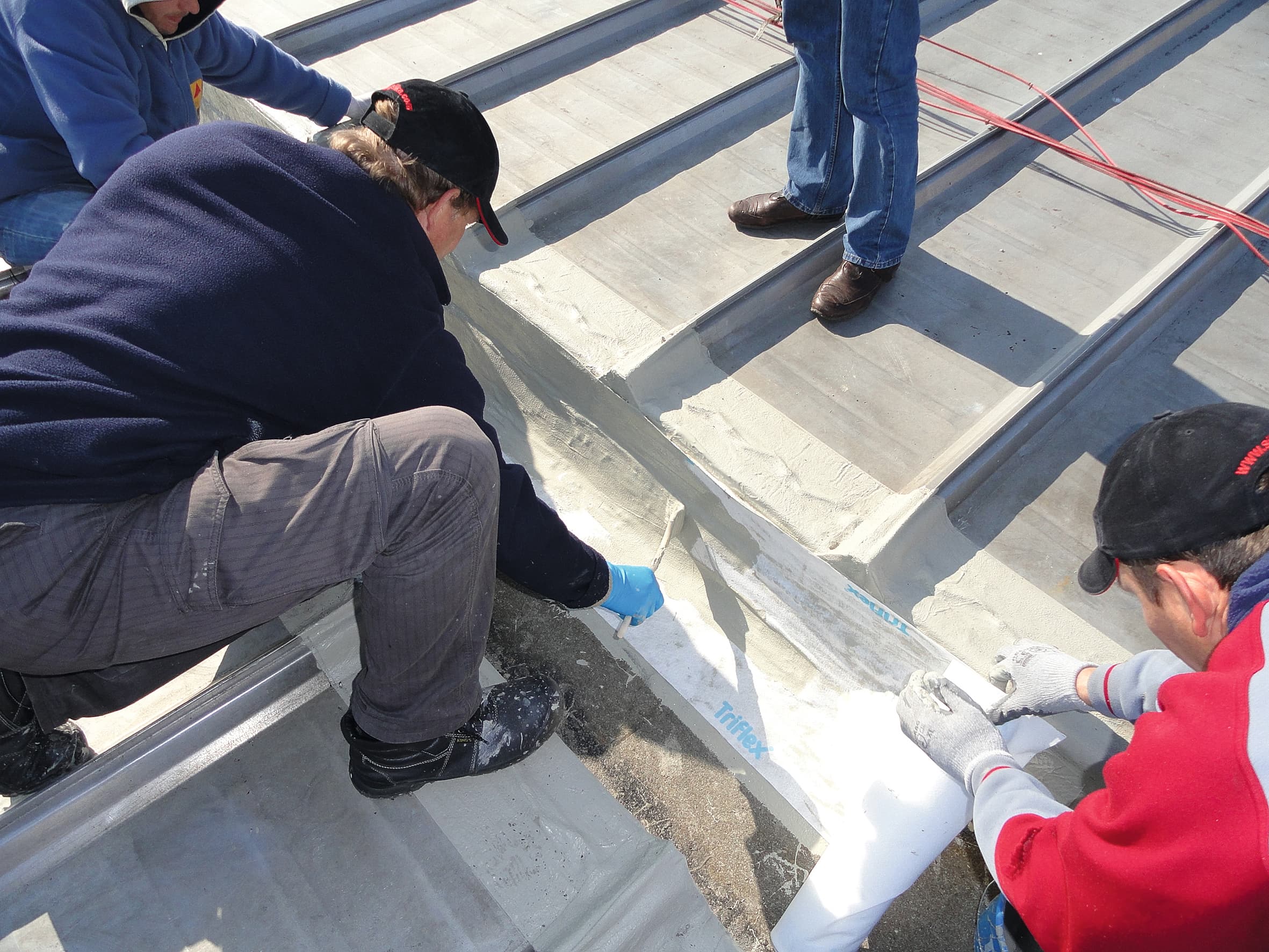 Fachkräfte tragen eine flüssig aufgebrachte Abdichtung auf einer Betontreppe im Außenbereich während der Bauausführung auf.
