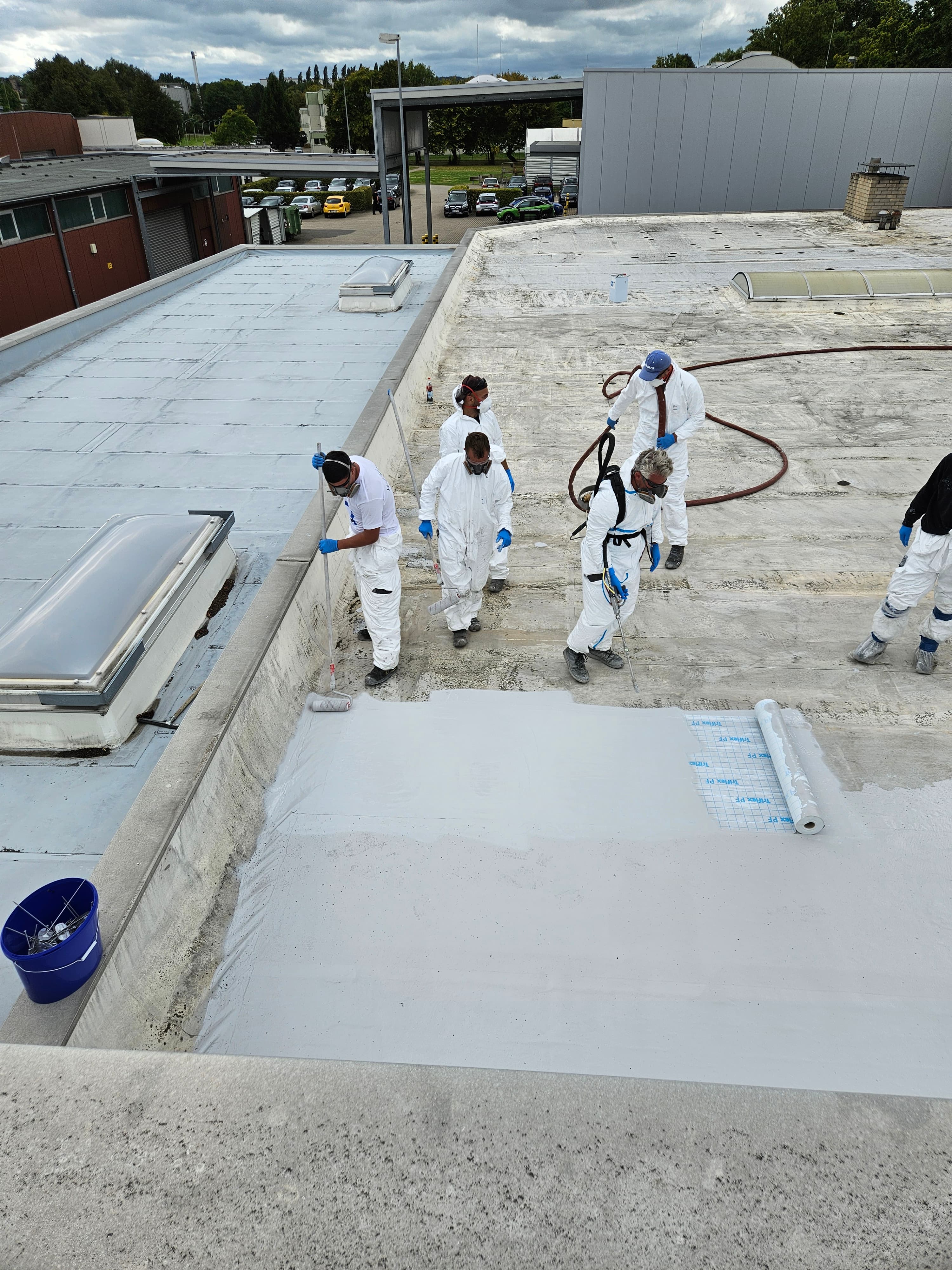 Several skilled workers applying a liquid-applied flat roof waterproofing system to an industrial building.