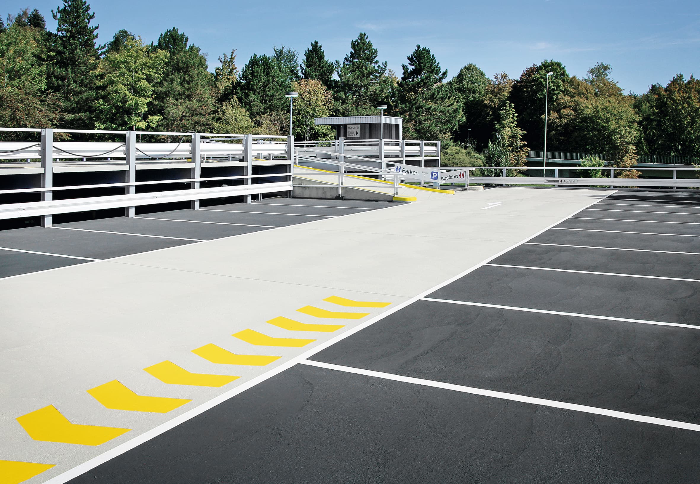Markierte Fahrgasse auf einem Parkdeck mit gelben Richtungs‑ und Bremsschwellenmarkierungen – funktionale Verkehrsflächenmarkierung für Parkhäuser.
