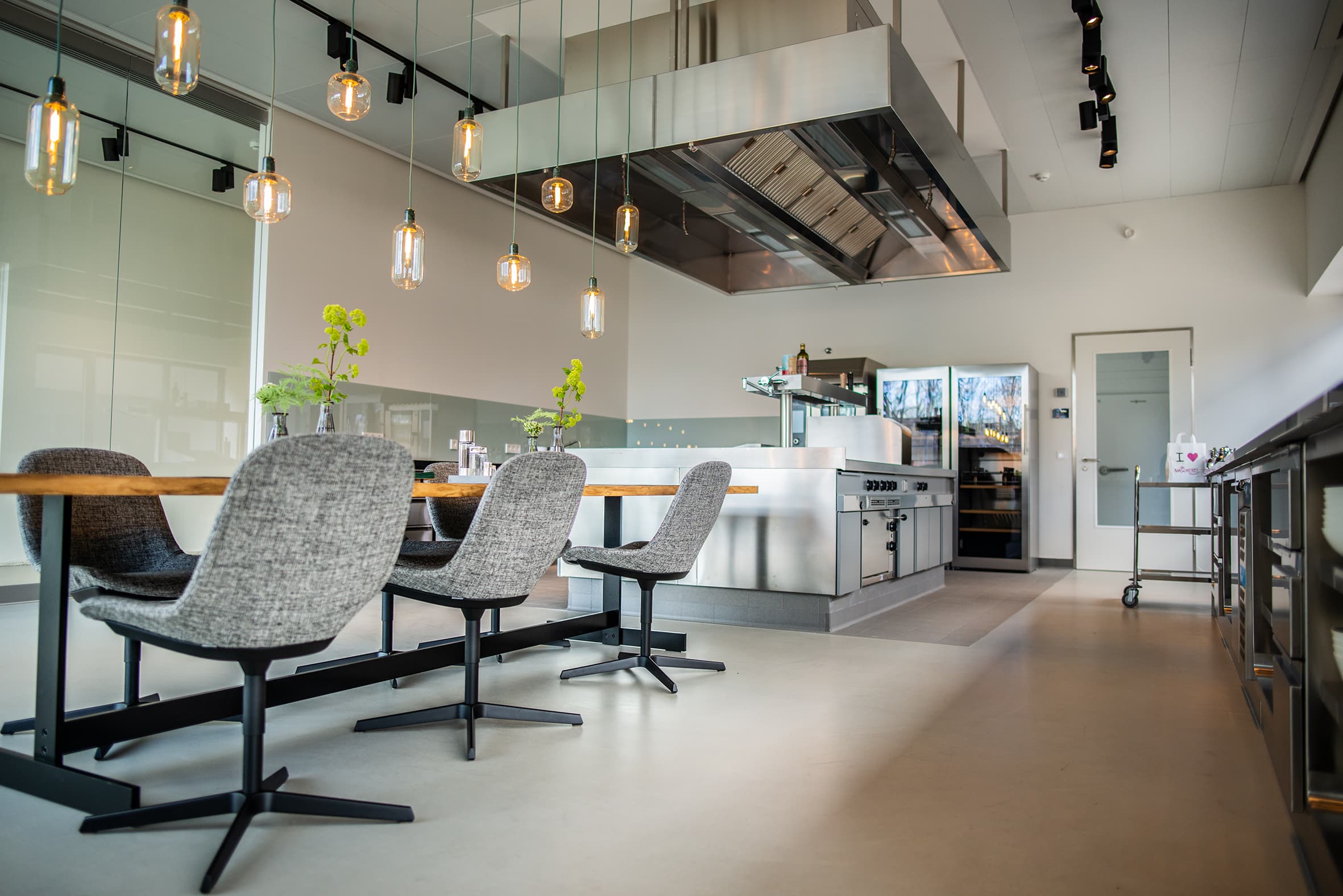 A modern lounge area with a coated floor, an open kitchen, and a seating area in an office building.