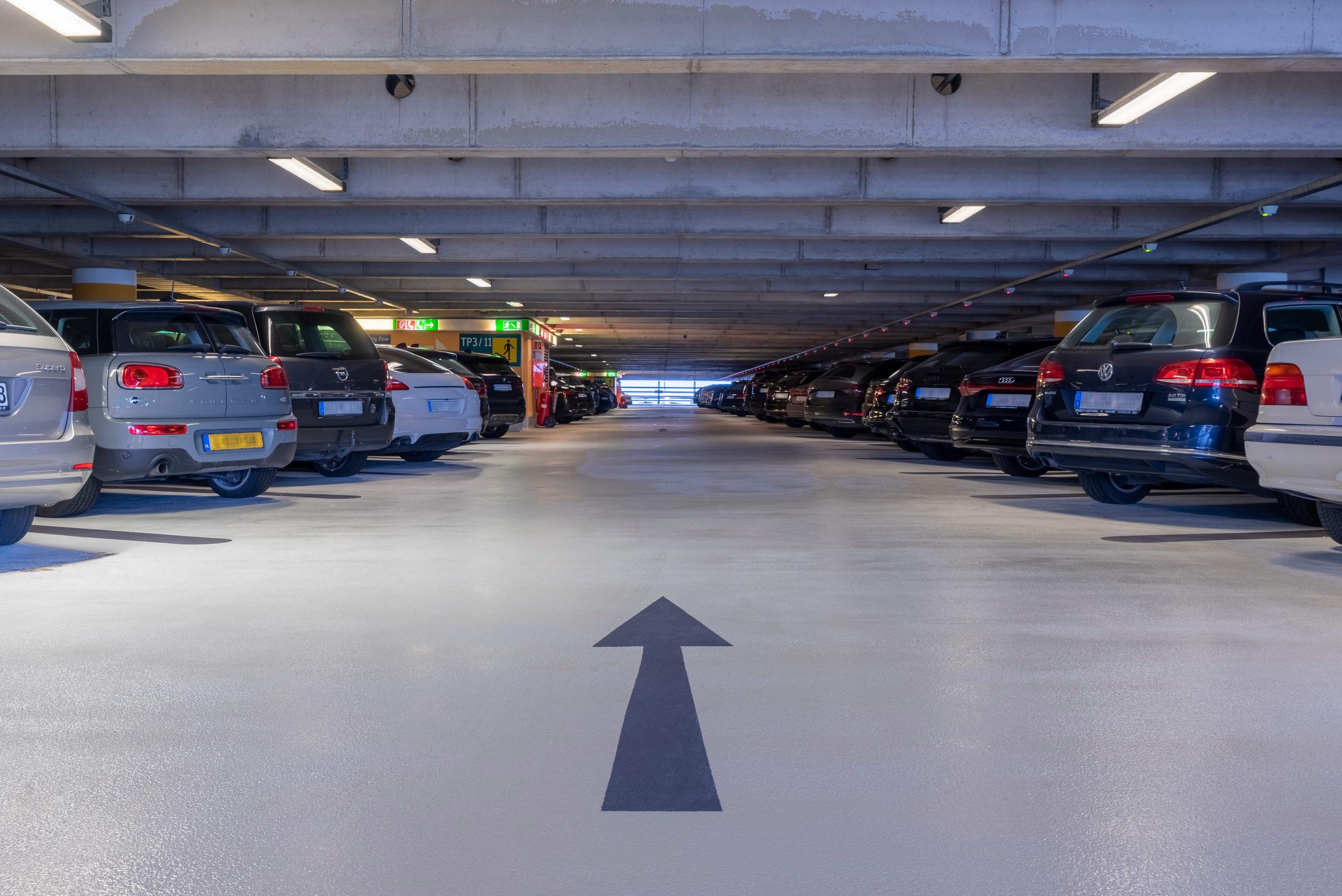Tiefgarage mit beschichteter Fahrbahn und aufgebrachter Richtungspfeil‑Markierung zwischen geparkten Fahrzeugen.