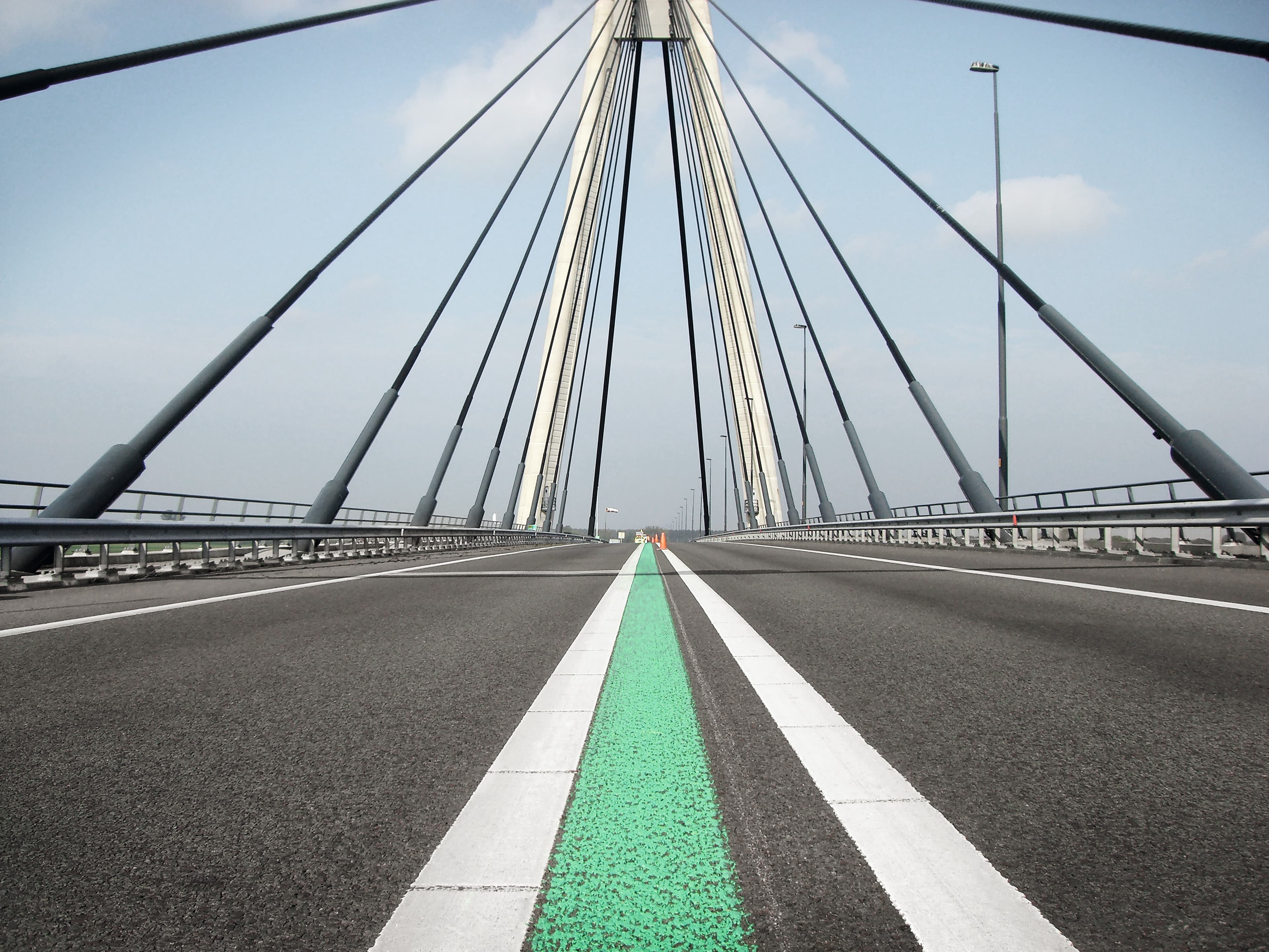 Zentrale Fahrbahn einer modernen Schrägseilbrücke mit markanter grüner Straßenmarkierung und klaren weißen Linien im urbanen Infrastrukturraum.