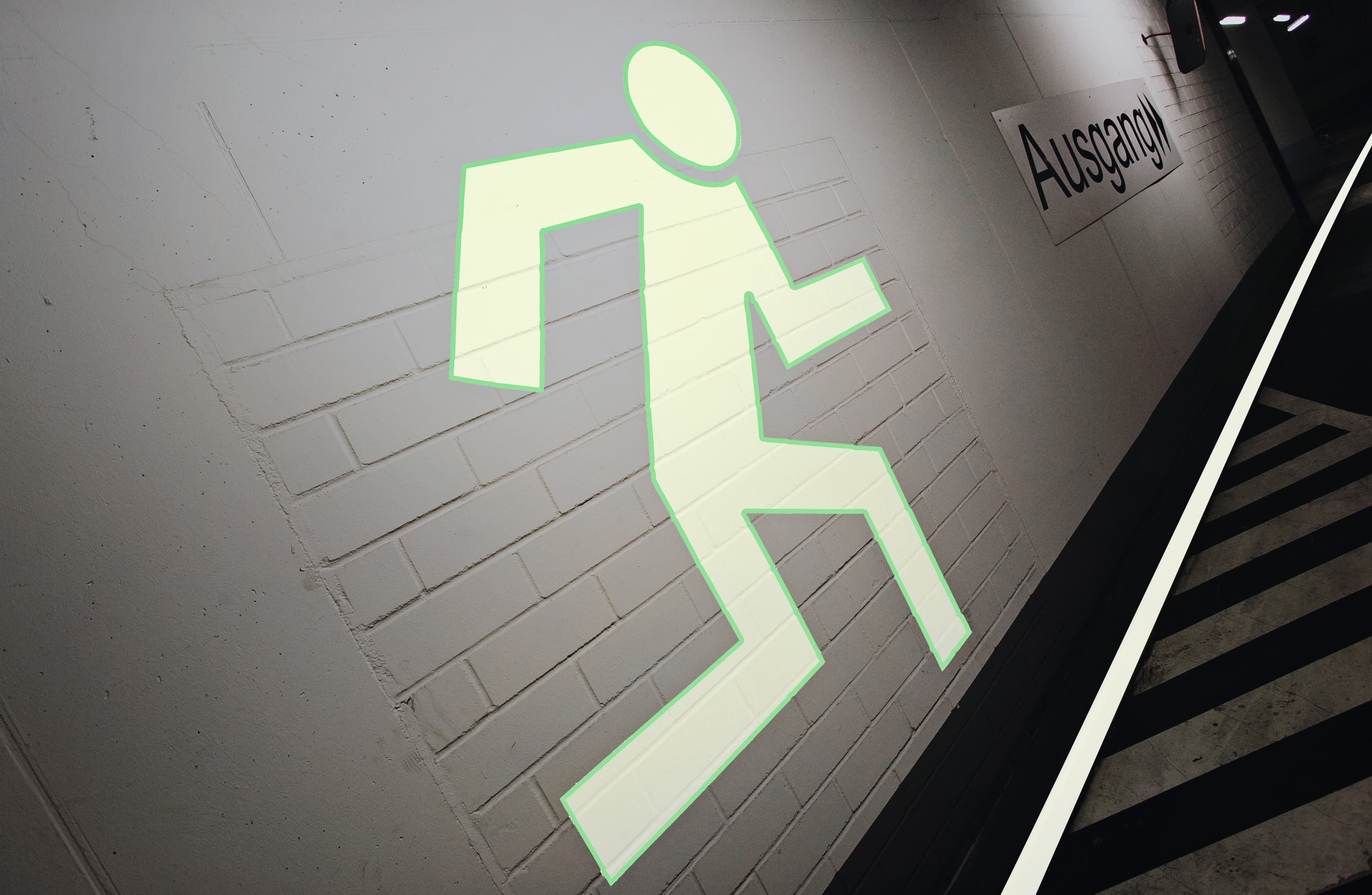 Fluchtwegkennzeichnung mit beleuchtetem Notausgang-Piktogramm an der Wand einer Tiefgarage
