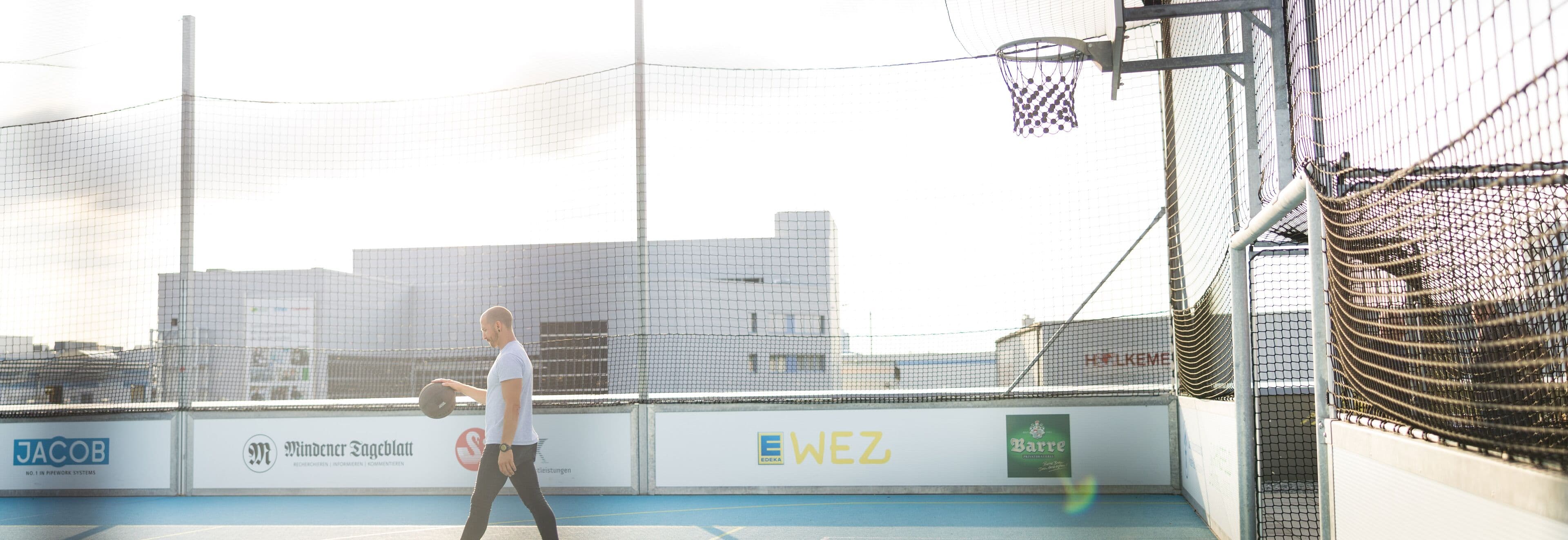 A rooftop sports area with a basketball hoop and a coated surface in an urban setting.
