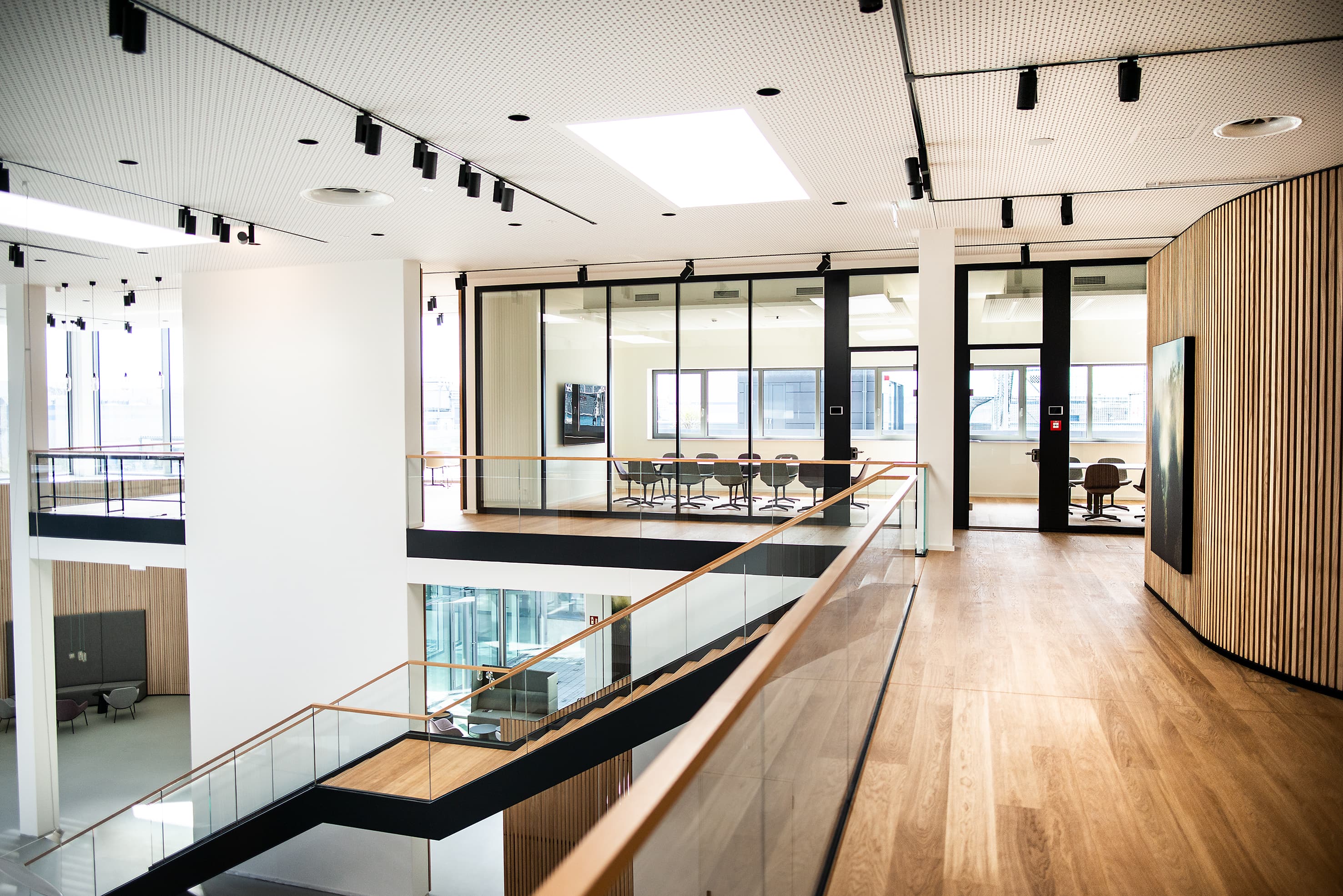 Modern interior of an office building featuring hardwood floors, glass railings, and an open gallery, showcasing high-quality architecture.