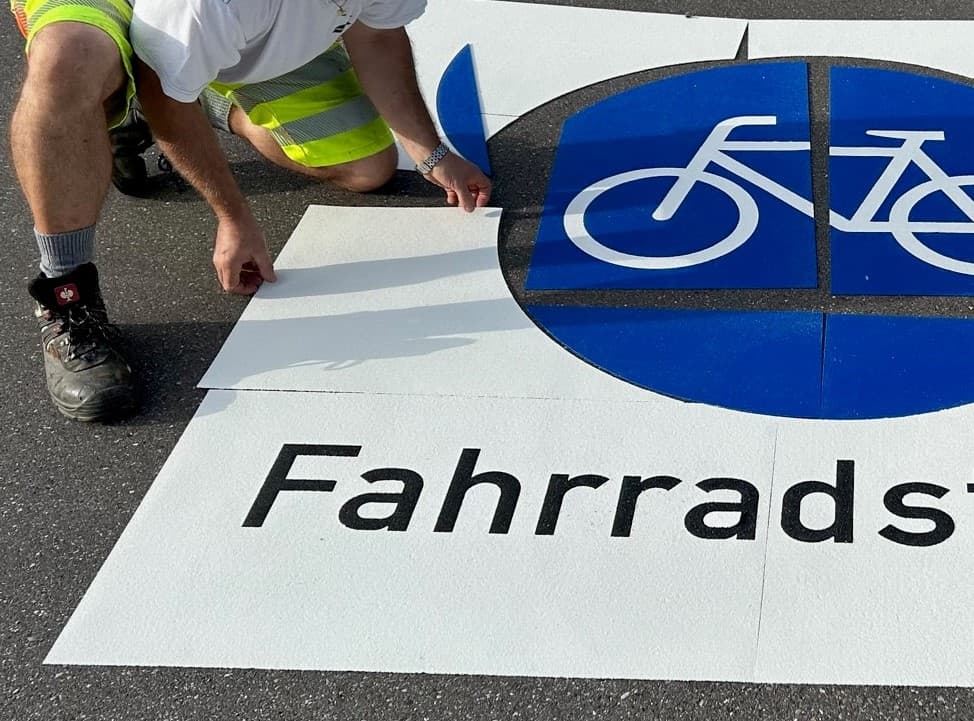 Aufbringen einer Bodenmarkierung für einen Fahrradweg mit Fahrradsymbol auf einer Verkehrsfläche.