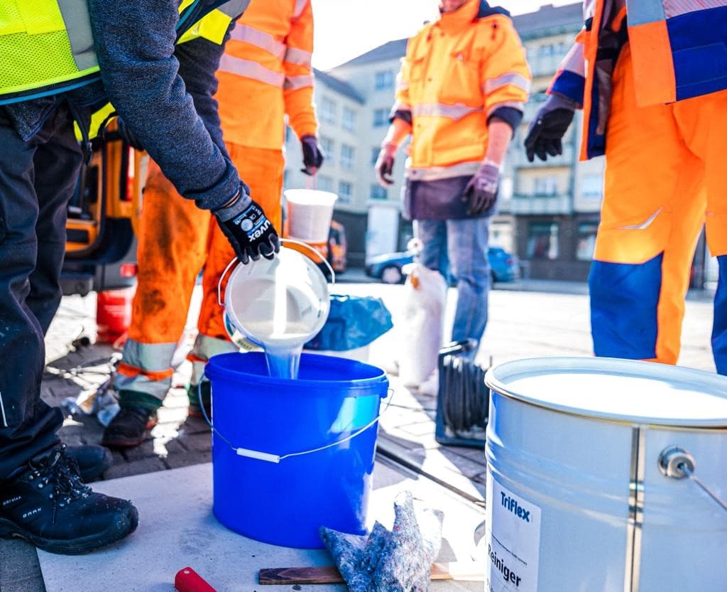 Hands-on training at a construction site with workers wearing high-visibility clothing as they mix a Triflex coating system