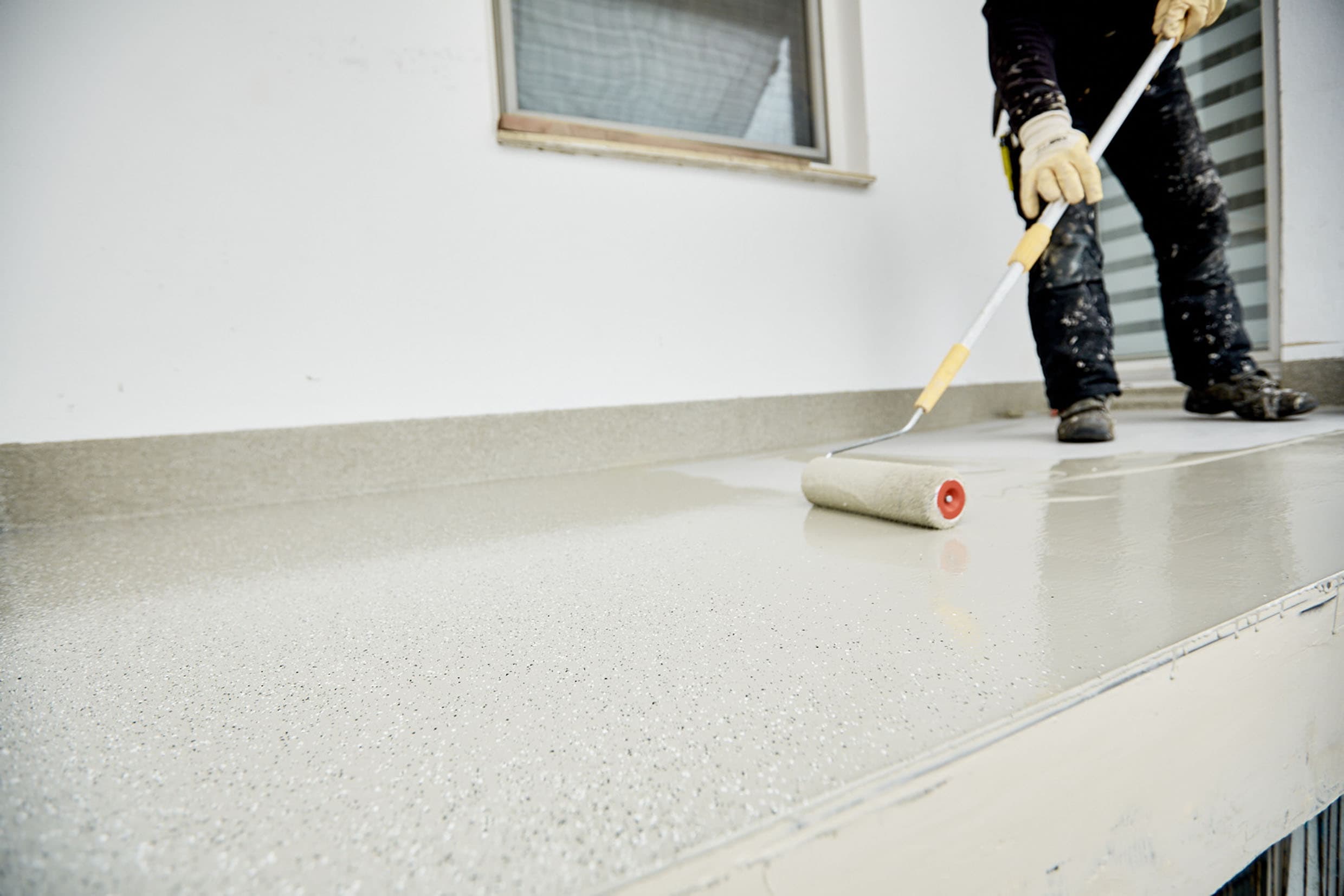Handwerker trägt Schutzbeschichtung auf eine Balkonfläche mit Roller auf – professionelle Balkonsanierung und Abdichtung.