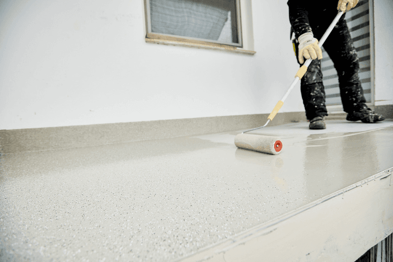 Handwerker trägt Schutzbeschichtung auf eine Balkonfläche mit Roller auf – professionelle Balkonsanierung und Abdichtung.