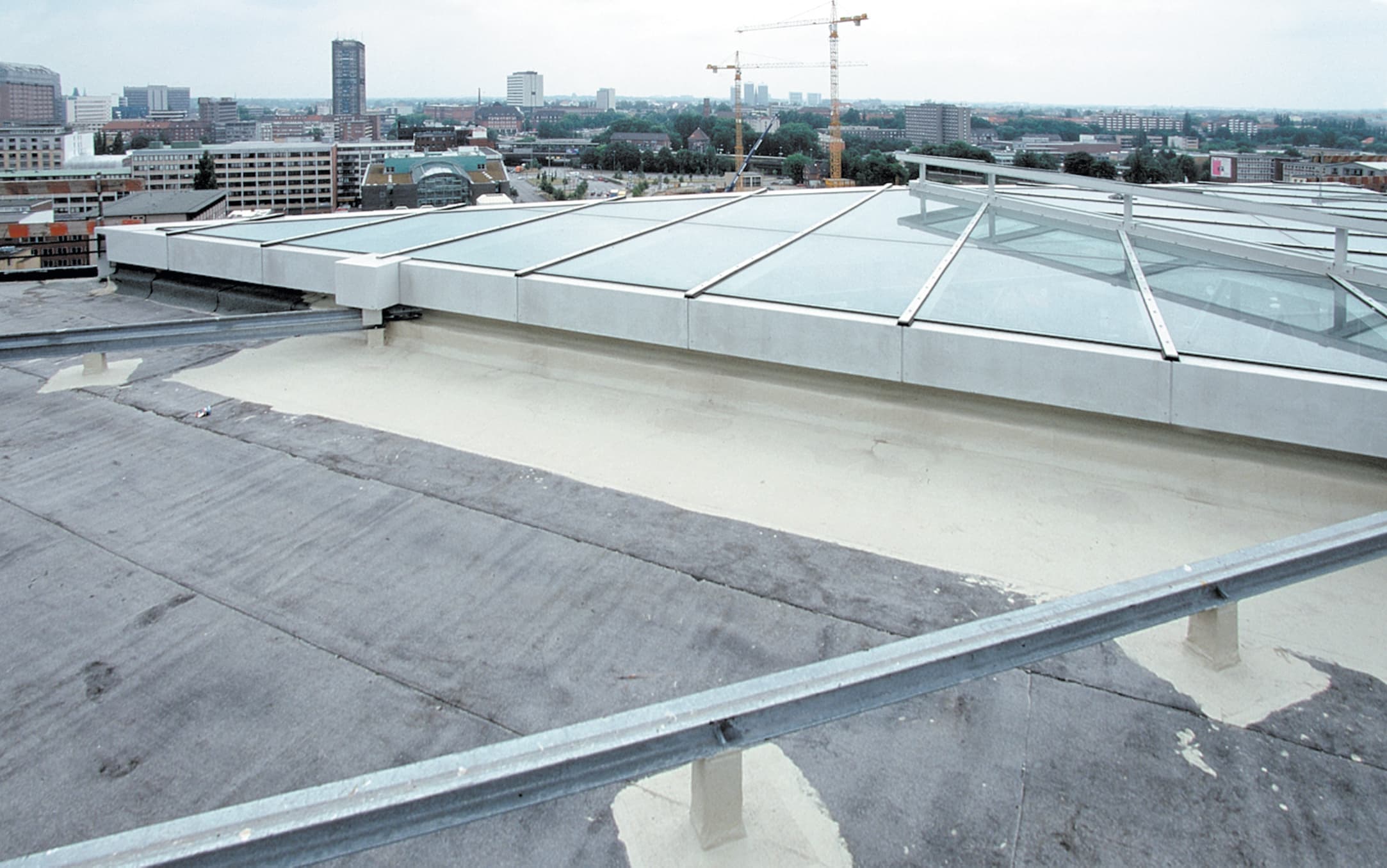 A flat roof with new waterproofing next to a large glass roof structure, photographed against an urban skyline.