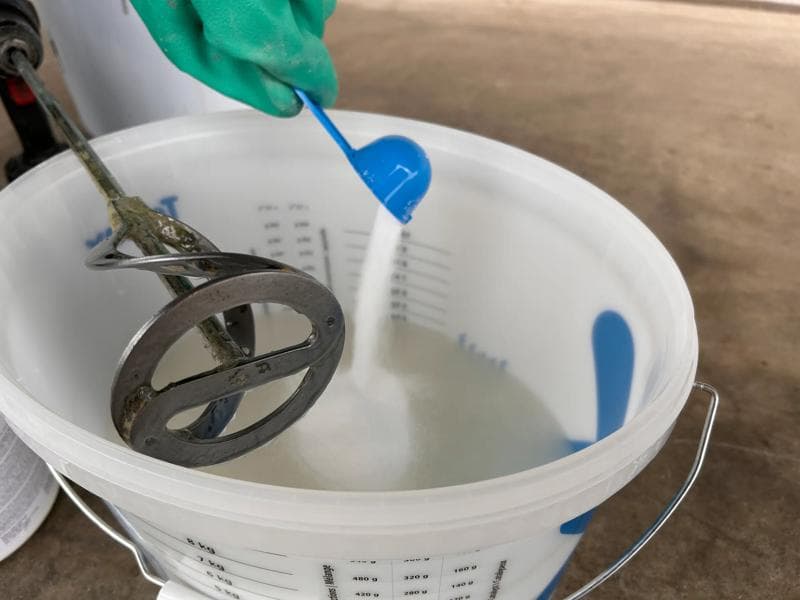 Pulverkomponente wird in Eimer mit Rührwerk zur Mischung gegeben