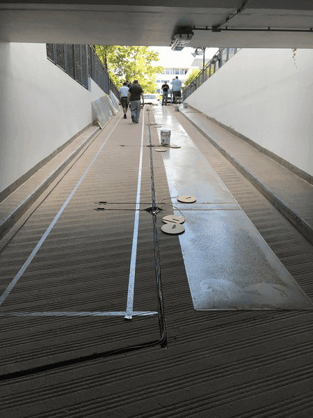 Sanierung einer Tiefgaragenzufahrt mit neuem Bodenbelag und markierten Führungsschienen; Handwerker arbeiten am oberen Rampenbereich.