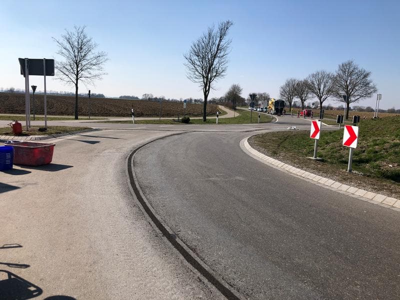 Asphaltierte Verkehrsfläche mit Fahrbahnmarkierung und Verkehrsinsel im ländlichen Umfeld