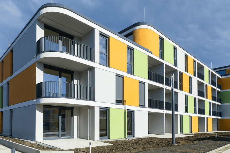 Modernes Mehrfamilienhaus mit farbiger Fassadengestaltung, Balkonen und zeitgemäßer Architektur nach Sanierung.