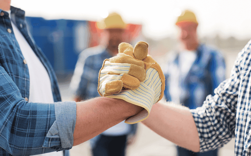 Handshake zweier Handwerker mit Arbeitshandschuhen als Symbol für Zusammenarbeit und Vertrauen auf der Baustelle