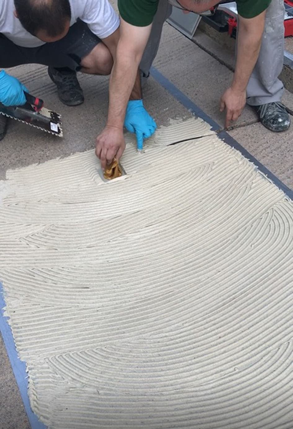Handwerker tragen mit Glättkelle frischen Mörtel auf vorbereitete Bodenfläche auf.