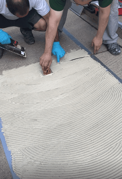 Handwerker tragen mit Glättkelle frischen Mörtel auf vorbereitete Bodenfläche auf.