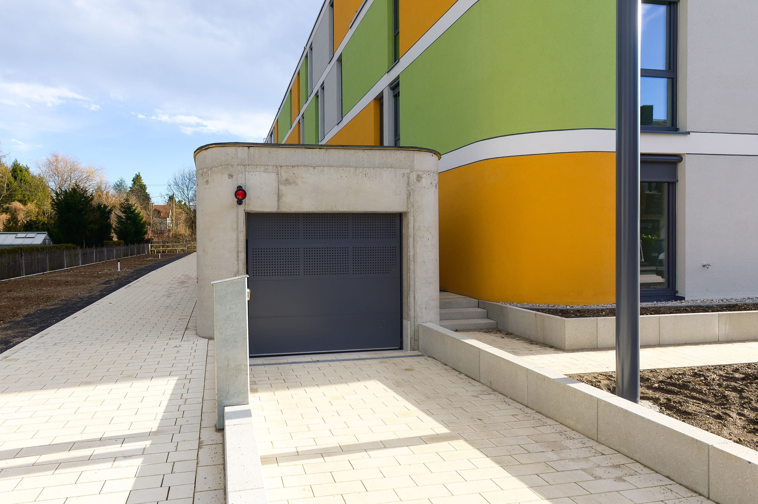 Zufahrt zu einer Tiefgarage mit modernem Rolltor und farbig gestalteter Gebäudefassade nach Sanierung.