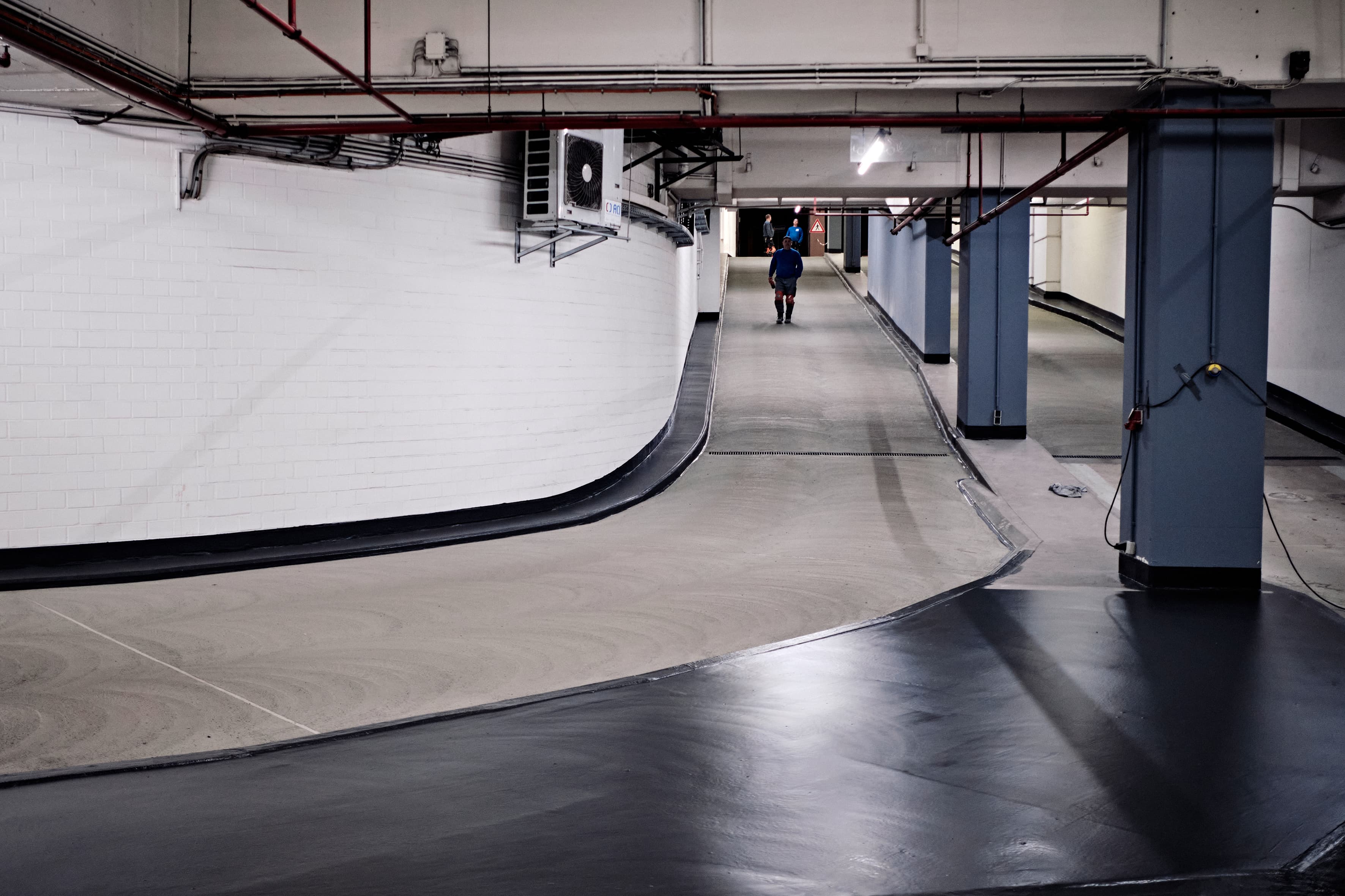 Sauber sanierter, hell beleuchteter Tiefgaragenbereich mit frisch beschichtetem Boden und klar abgegrenztem Fahrweg.