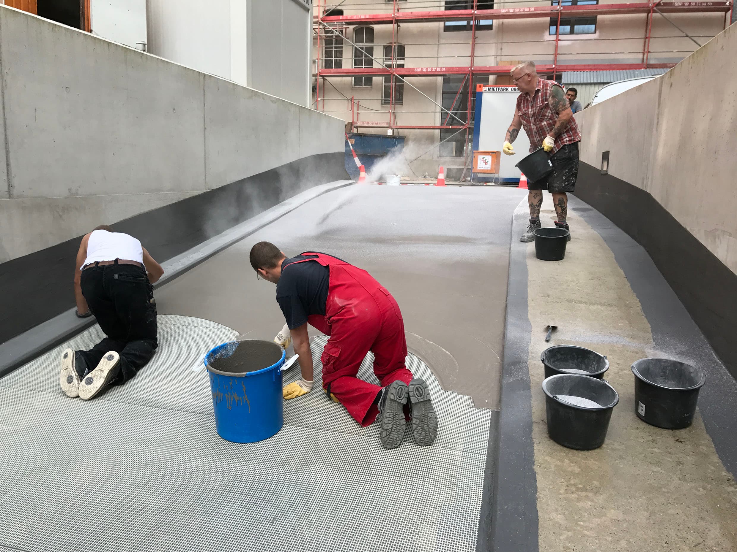 Handwerkliche Beschichtungsarbeiten auf einer Tiefgaragenrampe während der Bauphase, mit Auftragen und Glätten der Abdichtungsschicht.