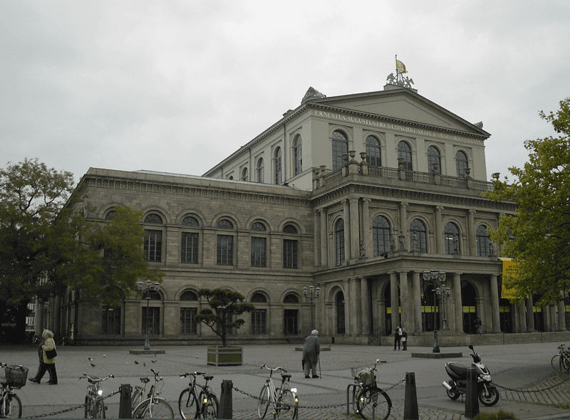 Historisches Opernhaus mit klassizistischer Fassade an einem städtischen Platz, Fahrräder und Passanten im Vordergrund.