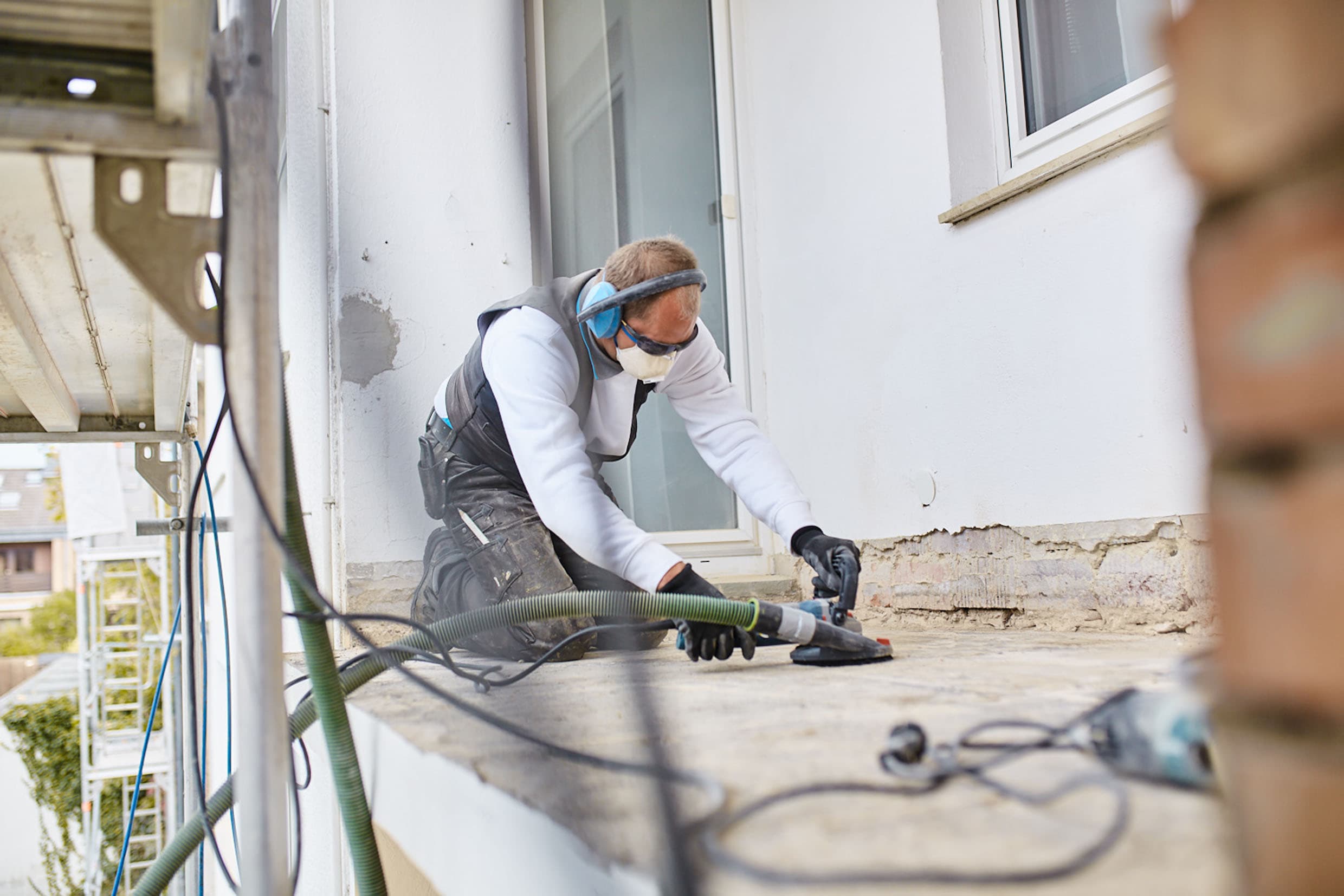 Fachkraft schleift schadhafte Betonfläche eines Balkons für eine Sanierung – professionelle Balkon‑Instandsetzung und Betonsanierung.