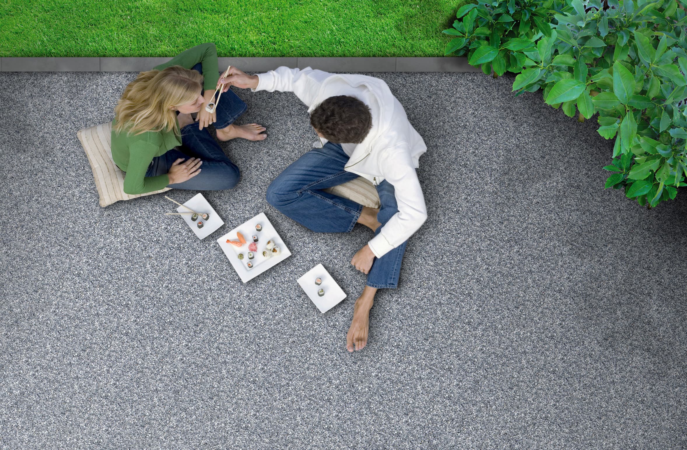 Pärchen sitzt auf einer Terrasse mit Triflex Stone Design Bodenbelag in Natursteinoptik und genießt gemeinsam Snacks