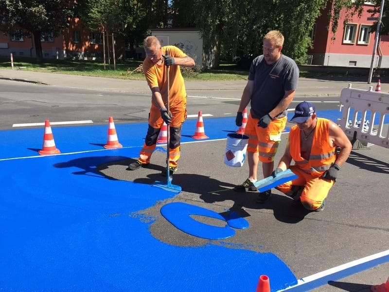 Fachkräfte tragen blaue Fahrbahnmarkierungsbeschichtung auf eine vorbereitete Straßenfläche auf.