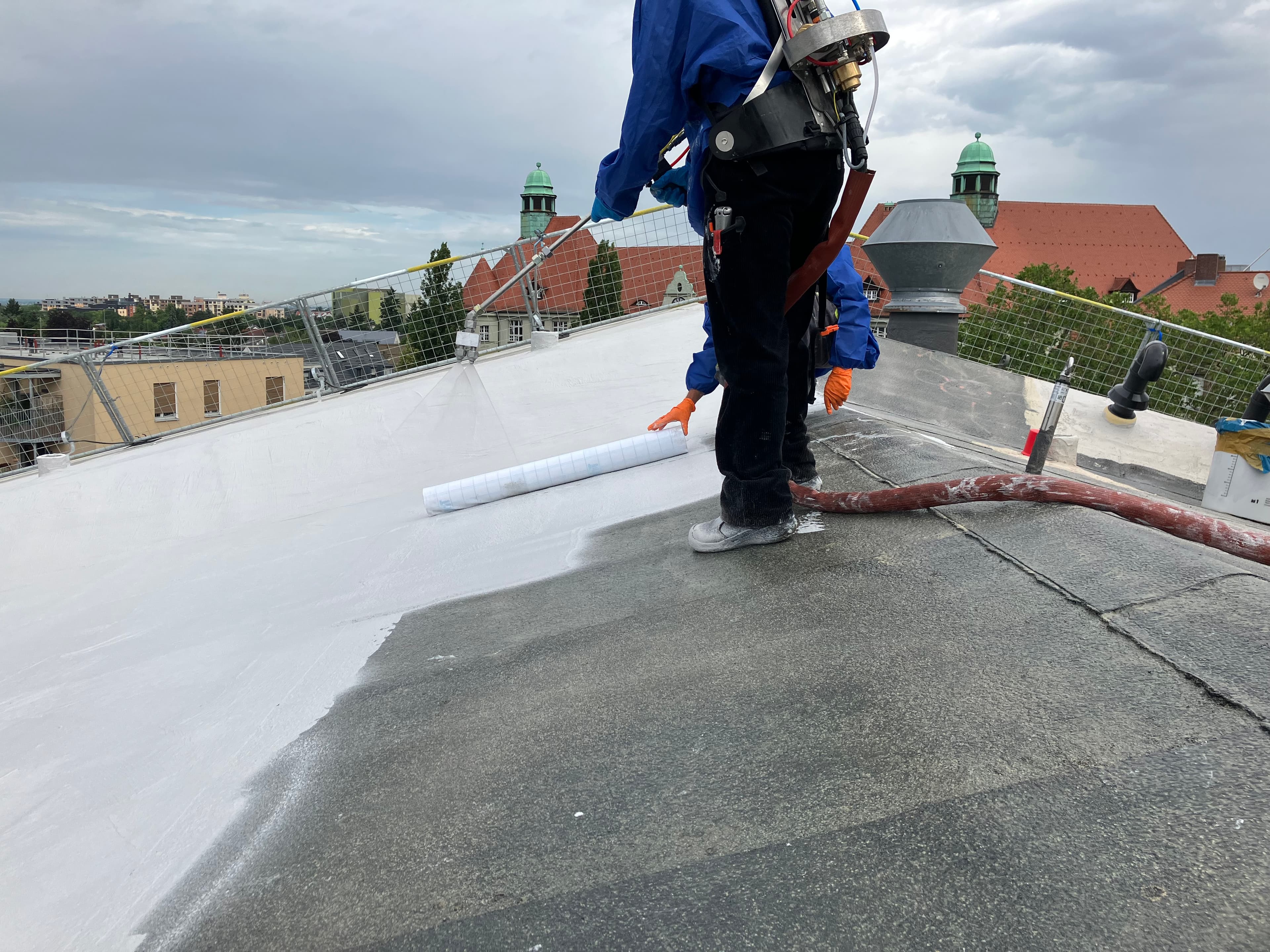 Workers renovating a gable roof in Berlin using Triflex ProTect roof waterproofing—applied with a roller and bucket.