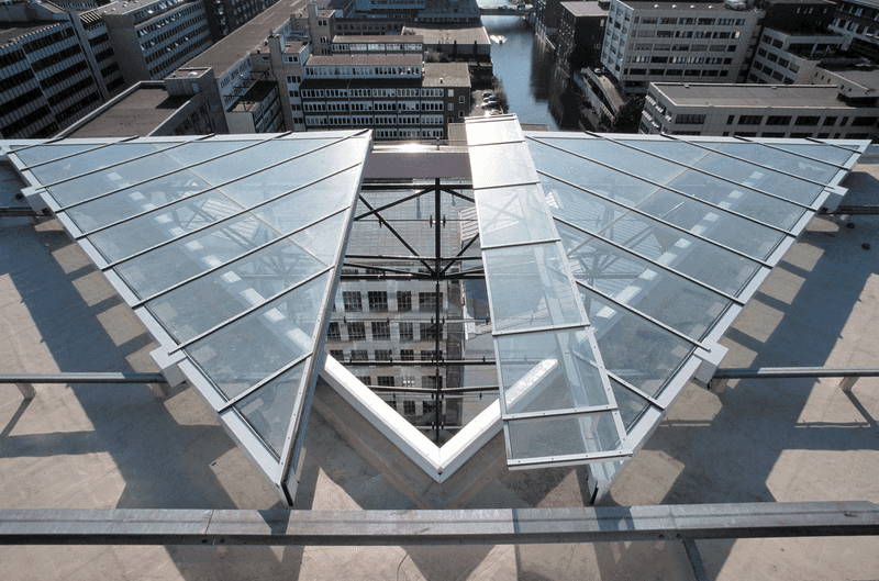 Dreiecksförmige Glasdachkonstruktion auf einem modernen Hochhaus, mit Blick über ein urbanes Büro- und Geschäftsviertel.